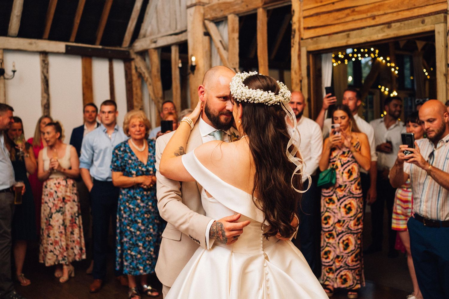 Wedding reception guests dance and celebrate in a rustic wooden barn venue decorated with string lights.