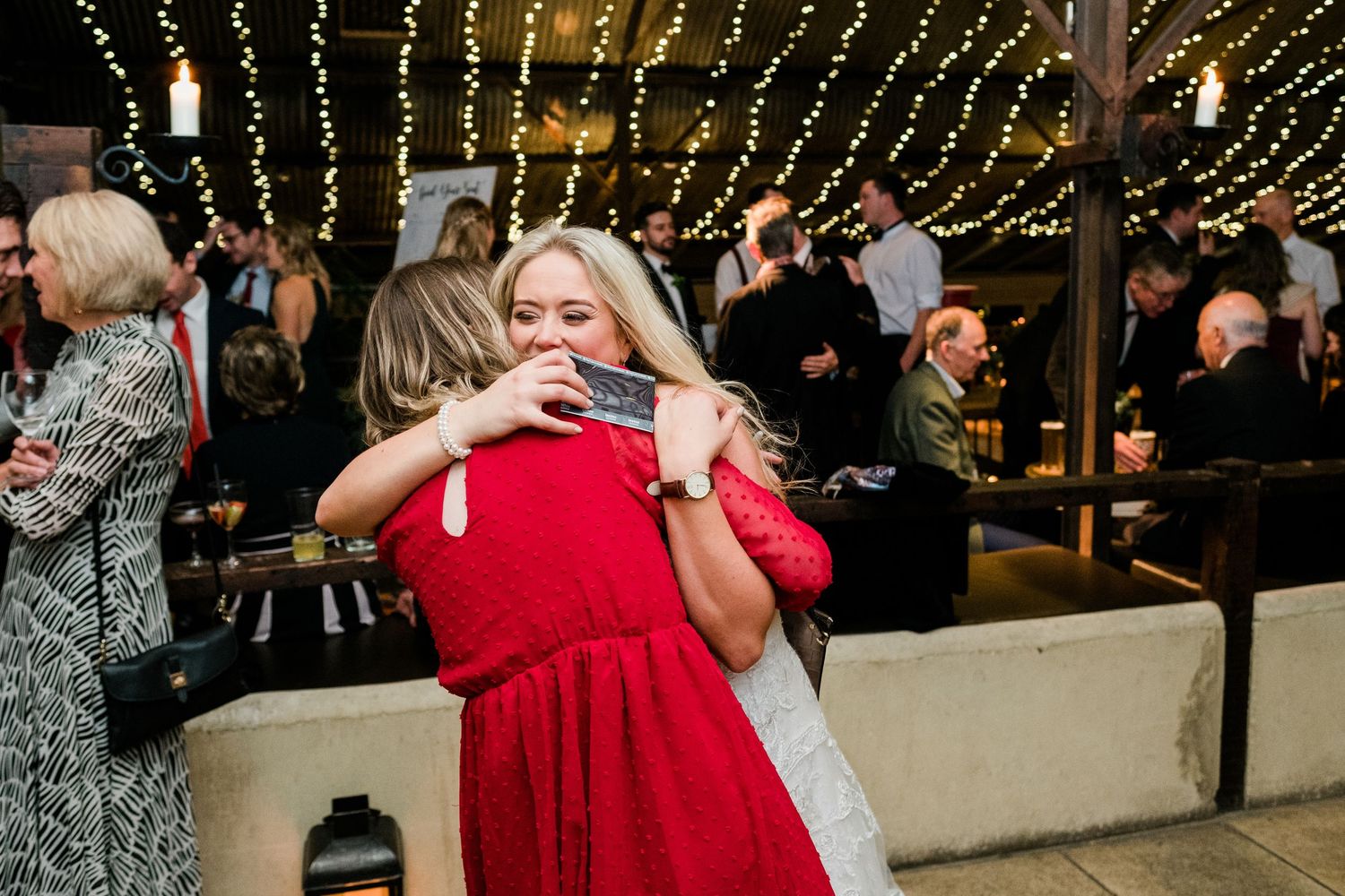 Wedding reception guests dancing and celebrating under romantic string lights at an evening venue.