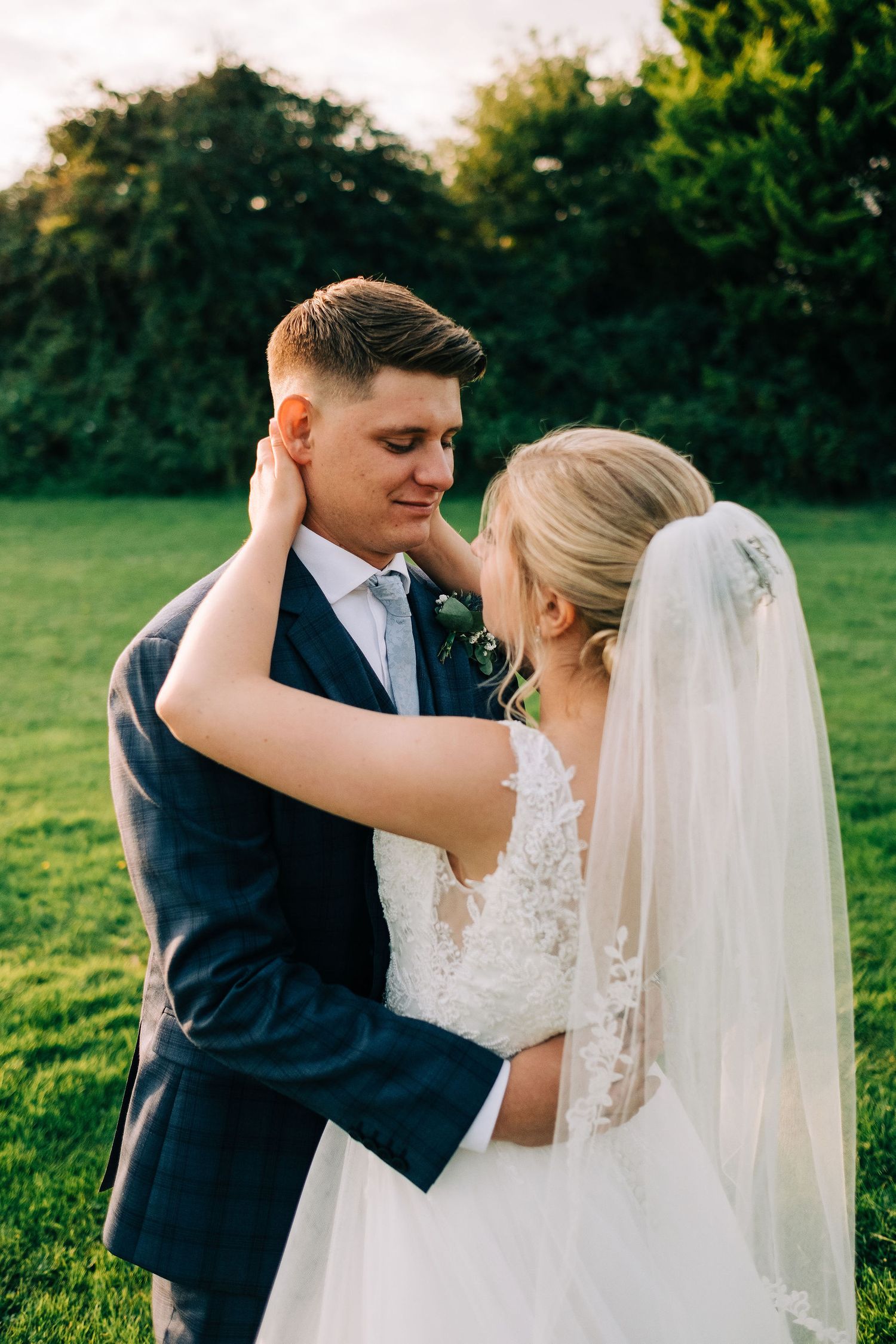 Newlywed couple sharing intimate moments in a sunlit green field during their wedding photoshoot.
