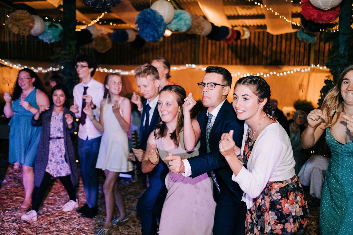 Wedding guests dancing and celebrating under string lights and blue decorations at an evening reception.