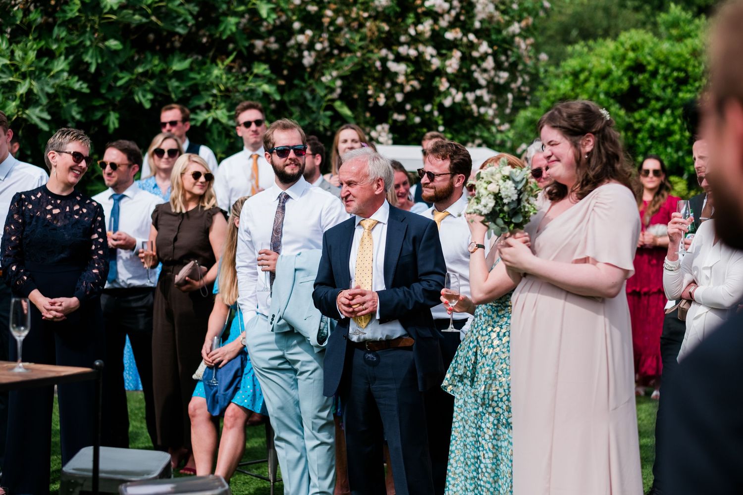 Guests in summer attire gather outdoors for a celebration in a garden setting.