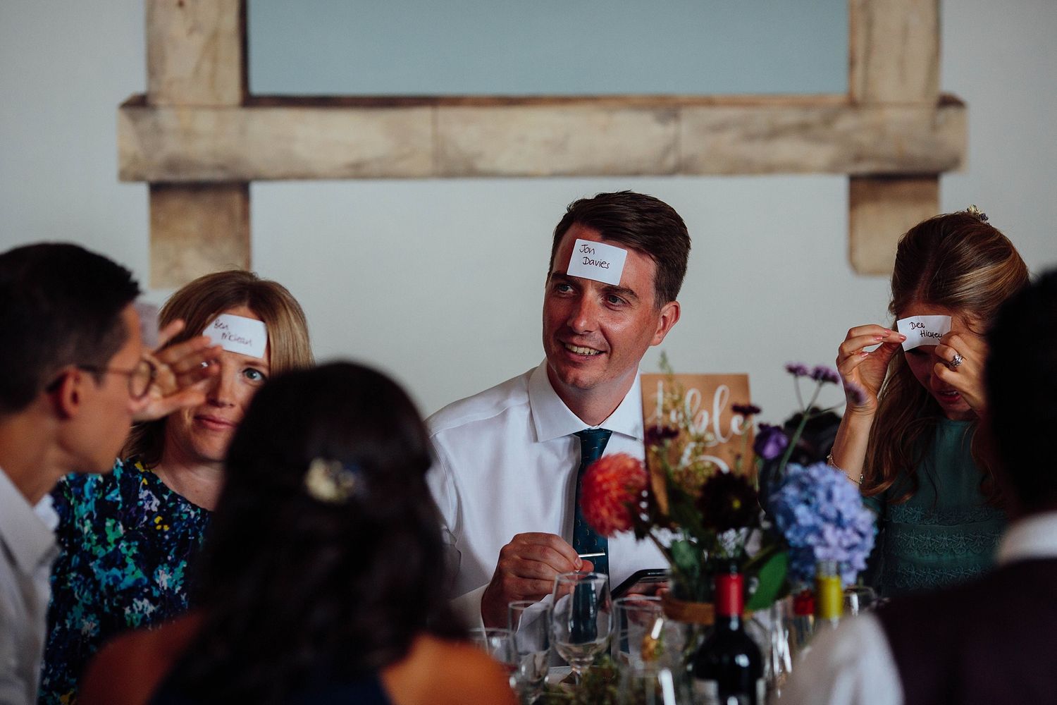 Wedding guests seated at rustic wooden tables during an indoor reception.