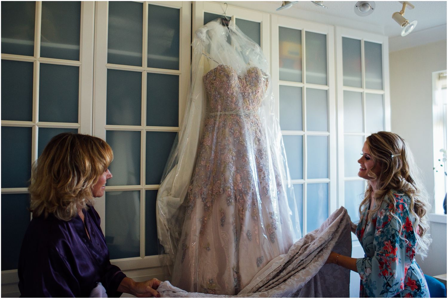 Two people admiring a wedding dress hanging in front of white closet doors.