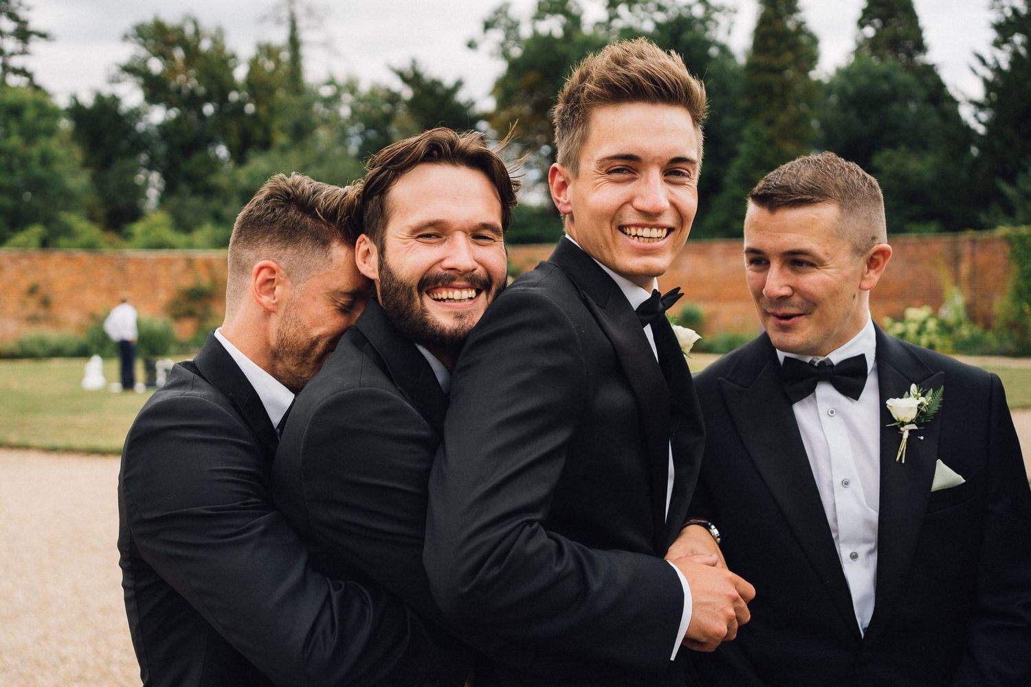 Groomsmen share laughs and celebrate during formal wedding photos outdoors.