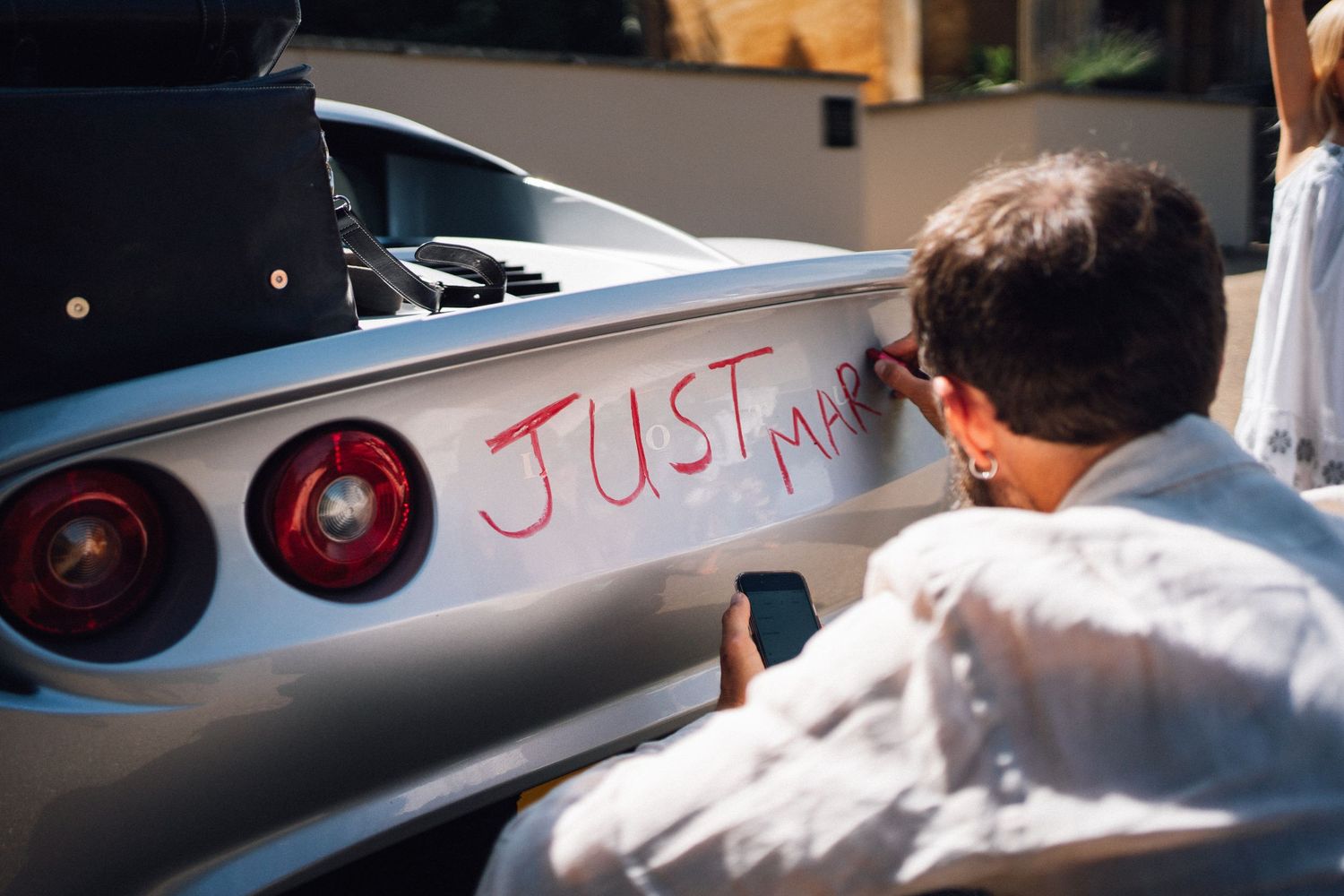 Someone writing 'Just' on a silver sports car's rear panel.