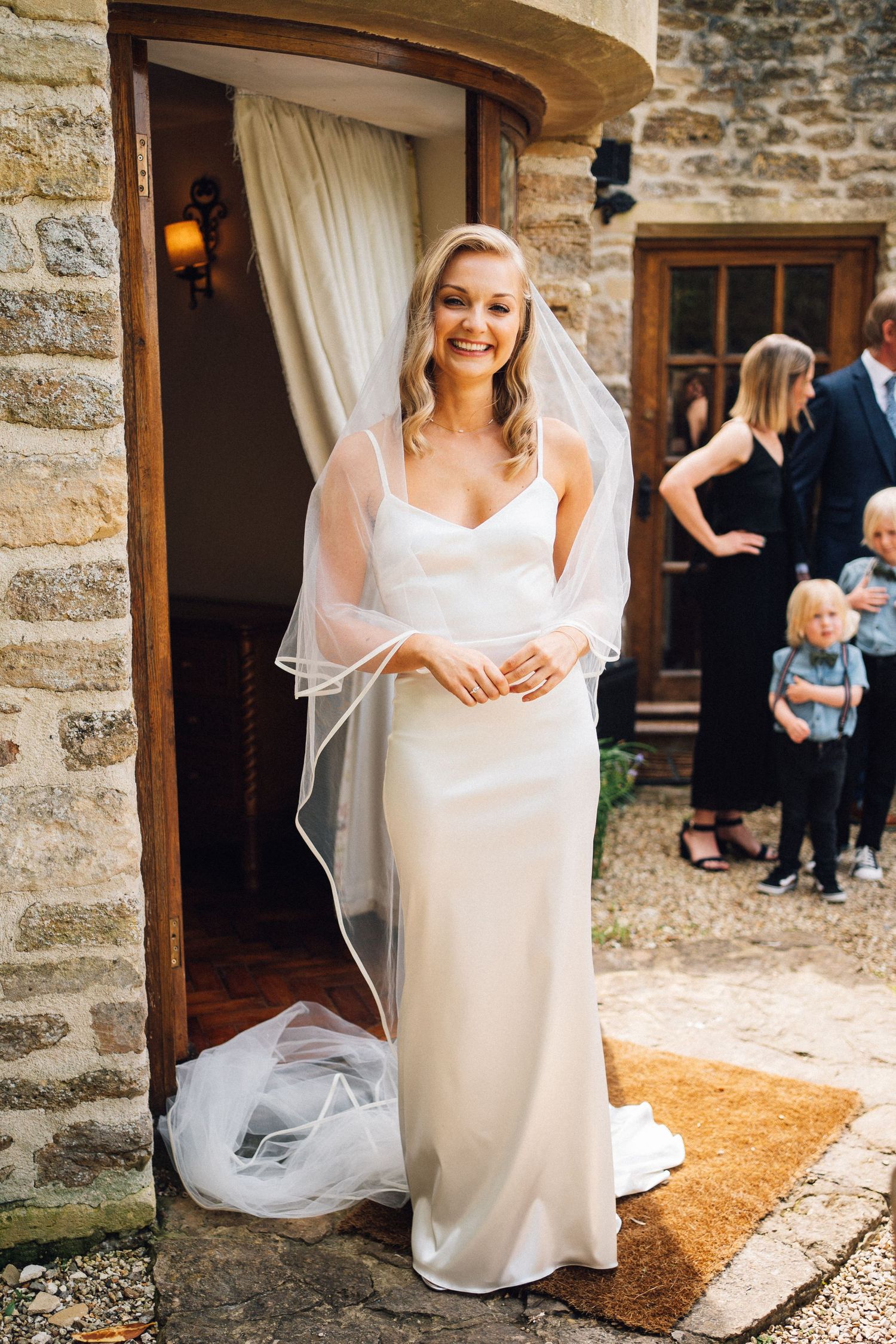Bride in flowing white dress and veil poses in front of stone building entrance.