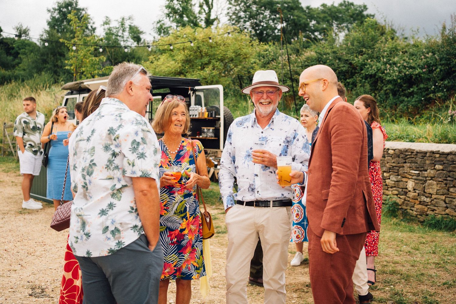 Wedding guests mingle in a garden setting wearing summer attire and floral patterns.