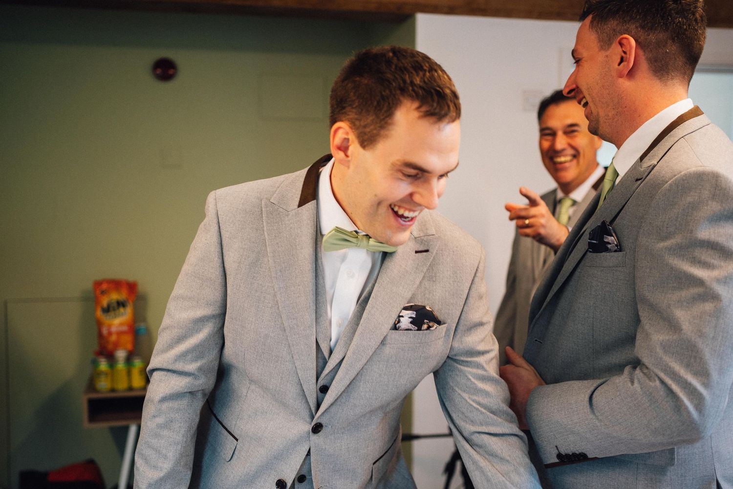 Wedding party members in light gray suits share laughs during pre-ceremony preparations.