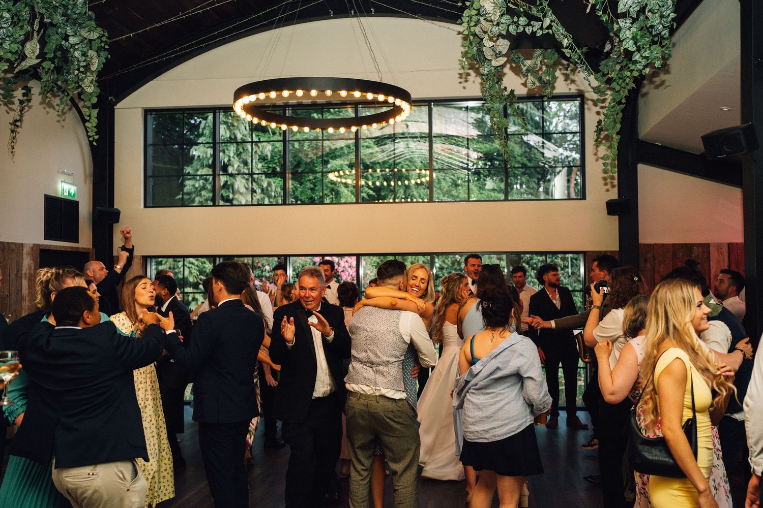 Panoramic view of a wedding reception venue with decorative lighting and greenery hanging from ceiling.