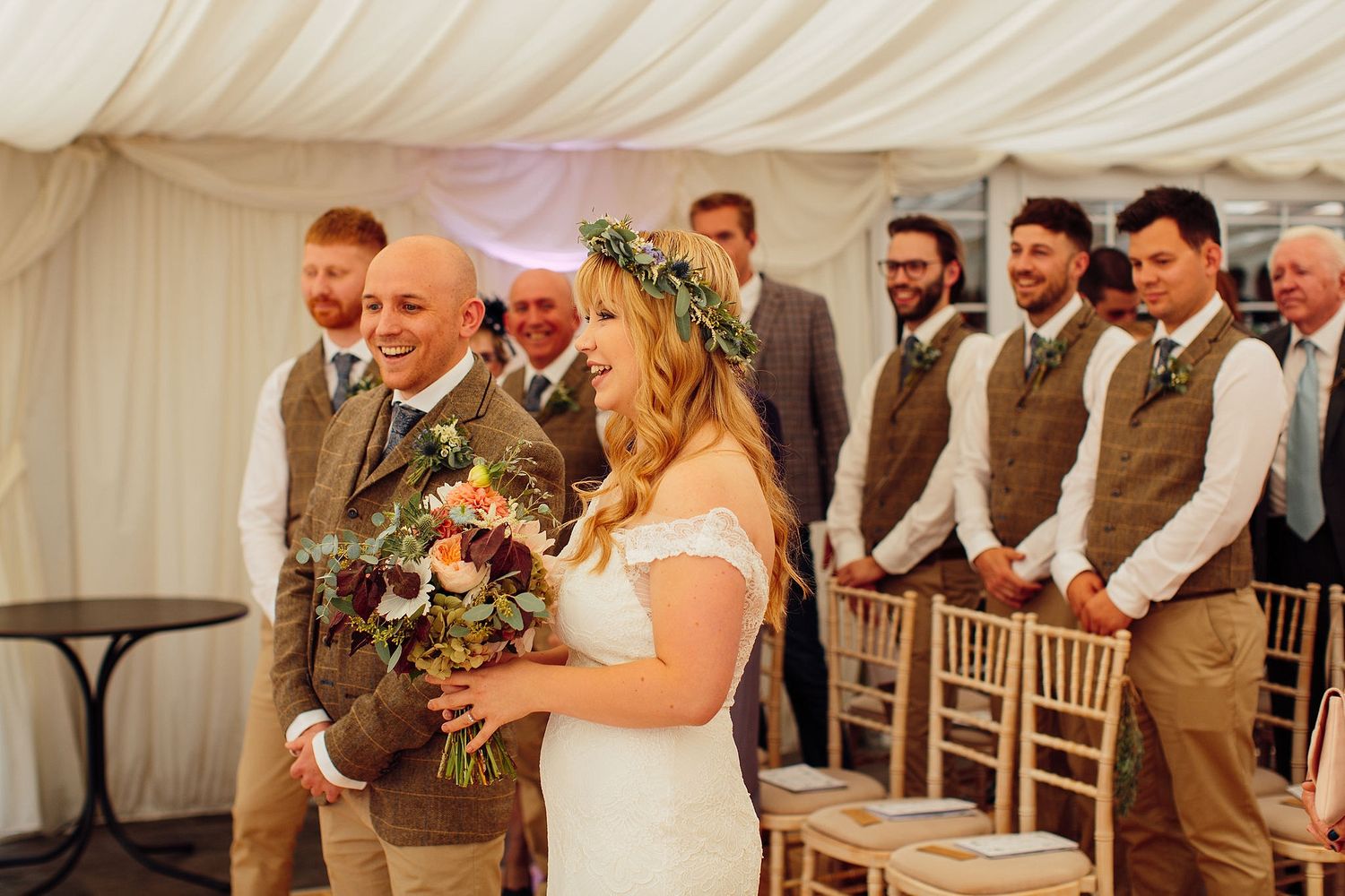 Elegant wedding reception under white draped tent with wooden chairs and floral accents.