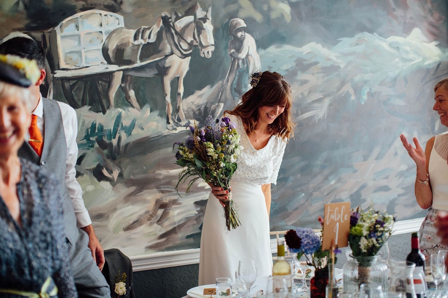 Wedding reception guests enjoying conversation at decorated tables with floral centerpieces.