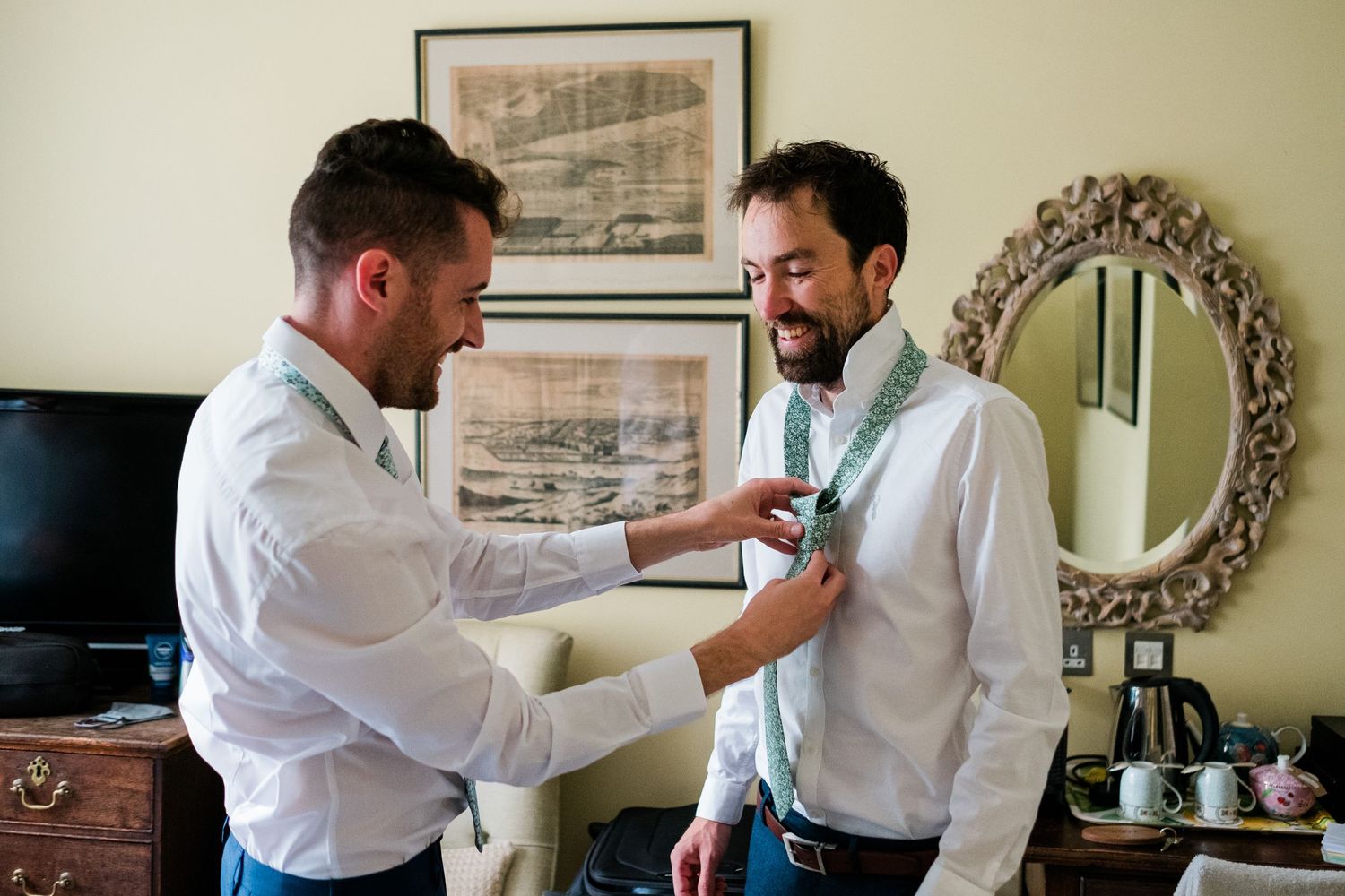 Two people in white dress shirts adjusting formal attire while getting ready for a special occasion.