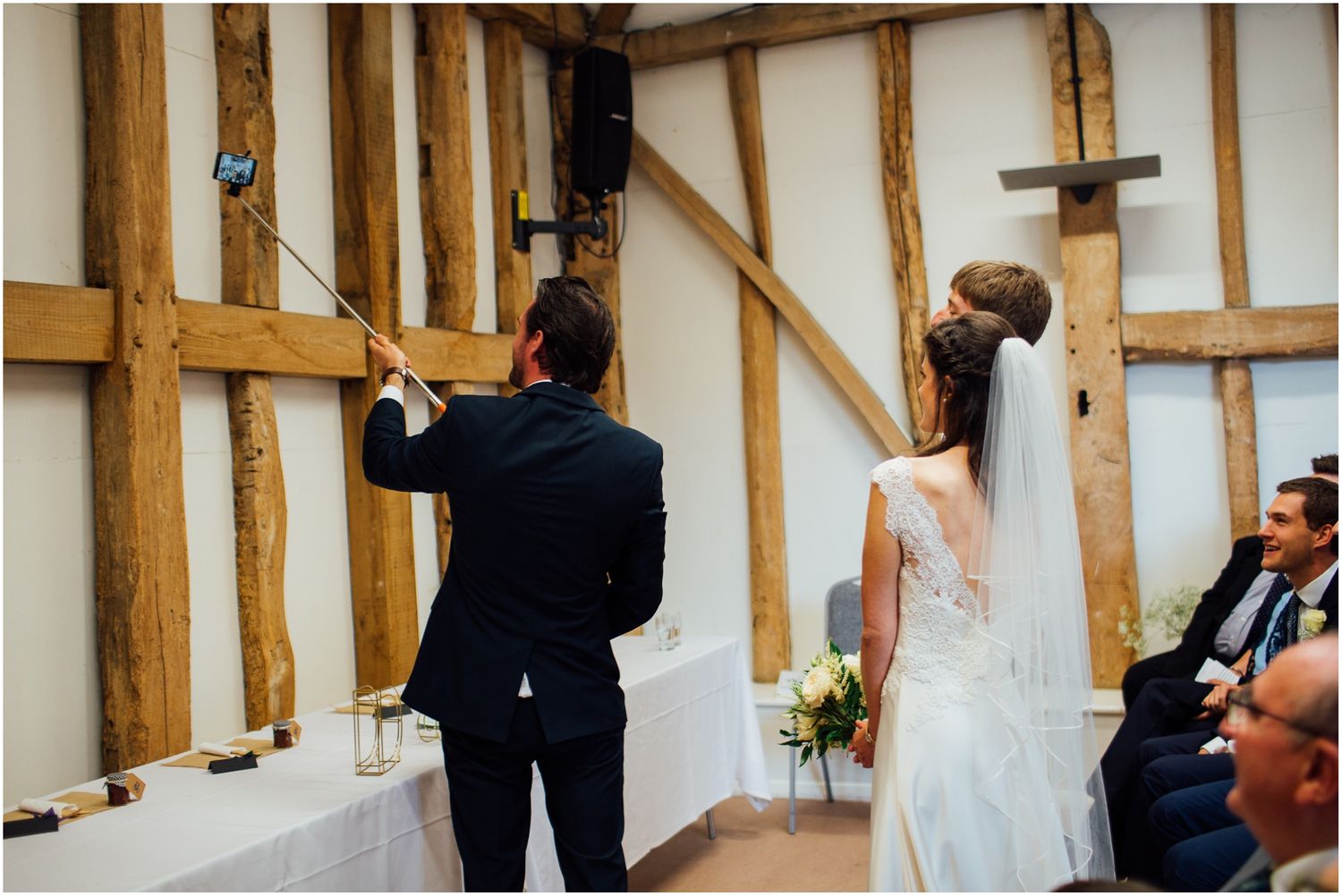 Wedding ceremony taking place in a rustic barn venue with exposed wooden beams and white walls.