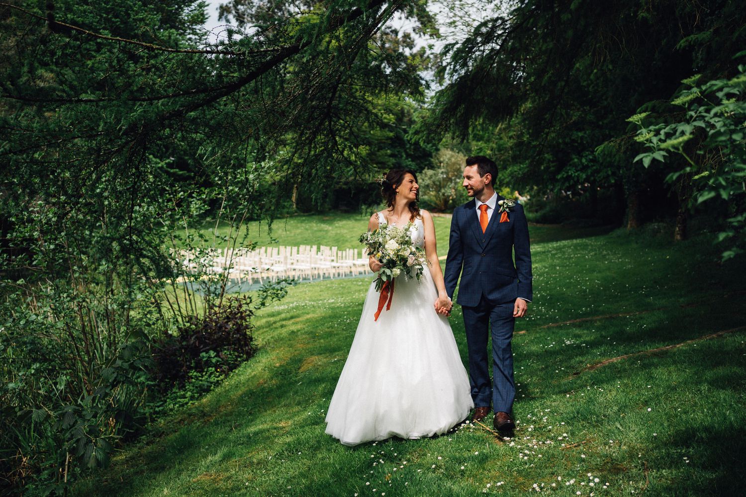 Newlyweds walk hand in hand through a scenic outdoor garden pathway.