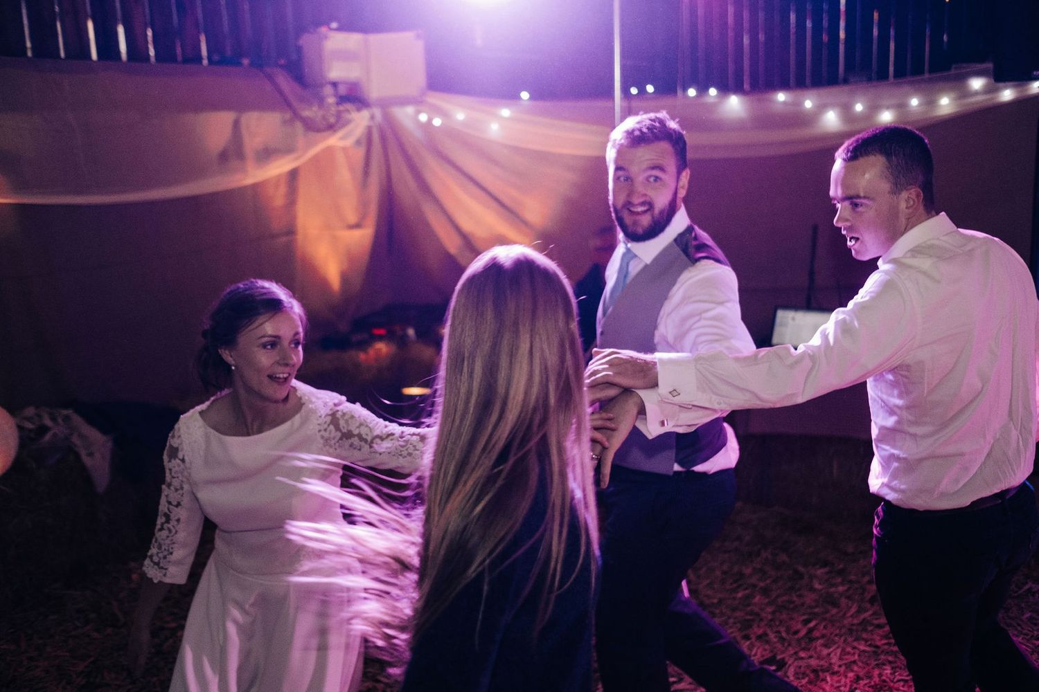 Wedding celebration on a dance floor with purple lighting and string lights overhead.