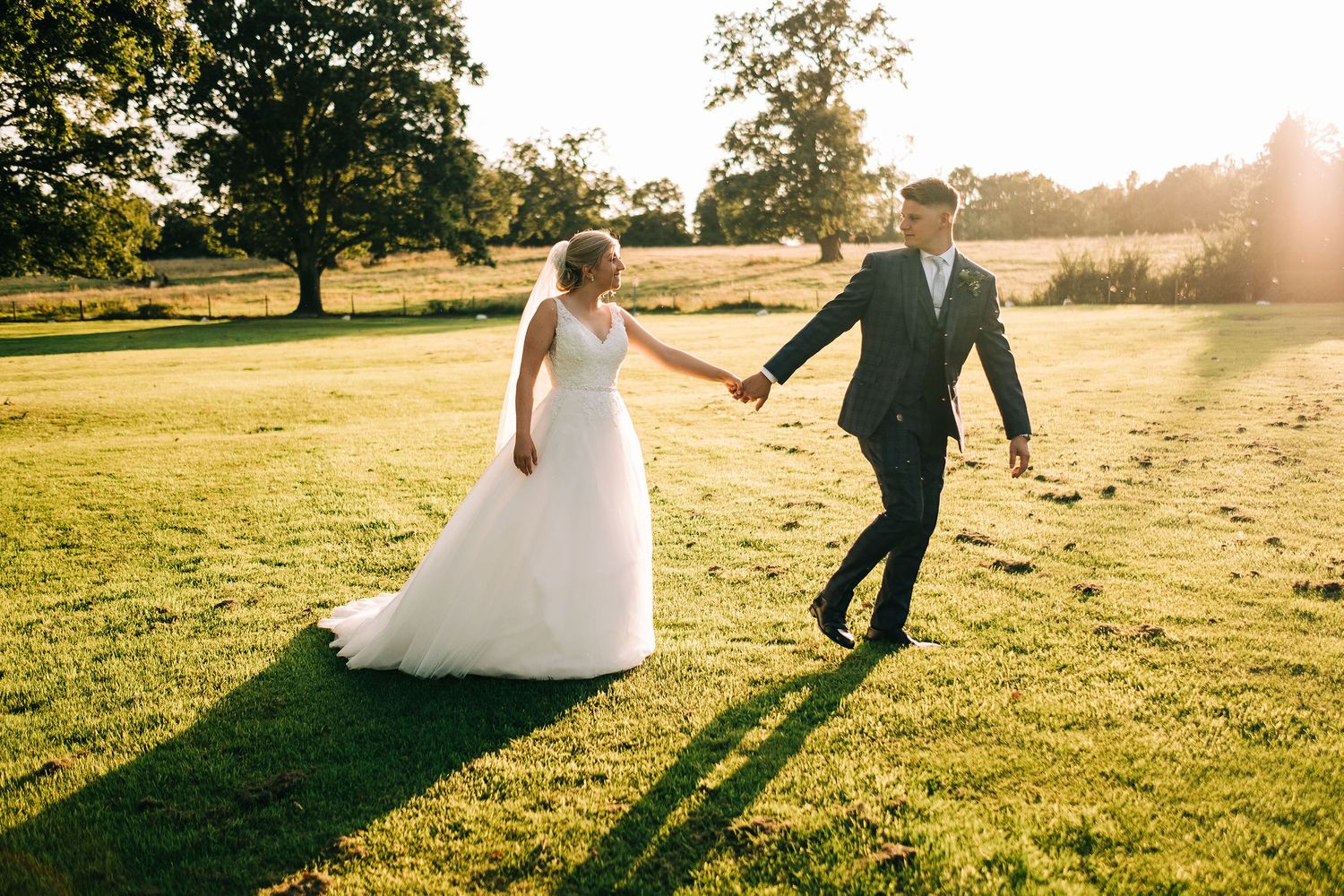 Joyful wedding couple walking through sun-drenched field at golden hour.
