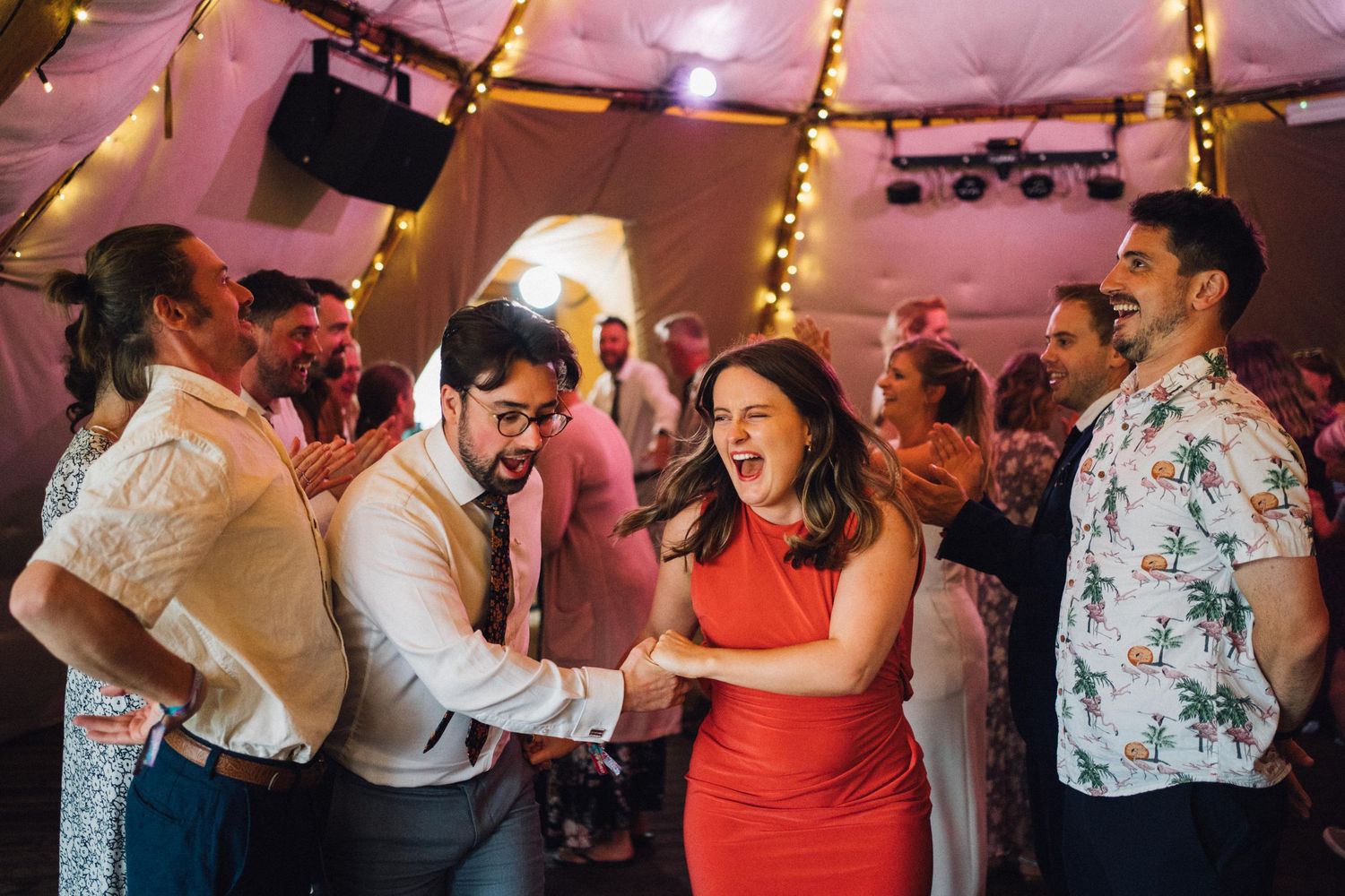 People dancing and celebrating at a lively indoor party with pink lighting and festive atmosphere.