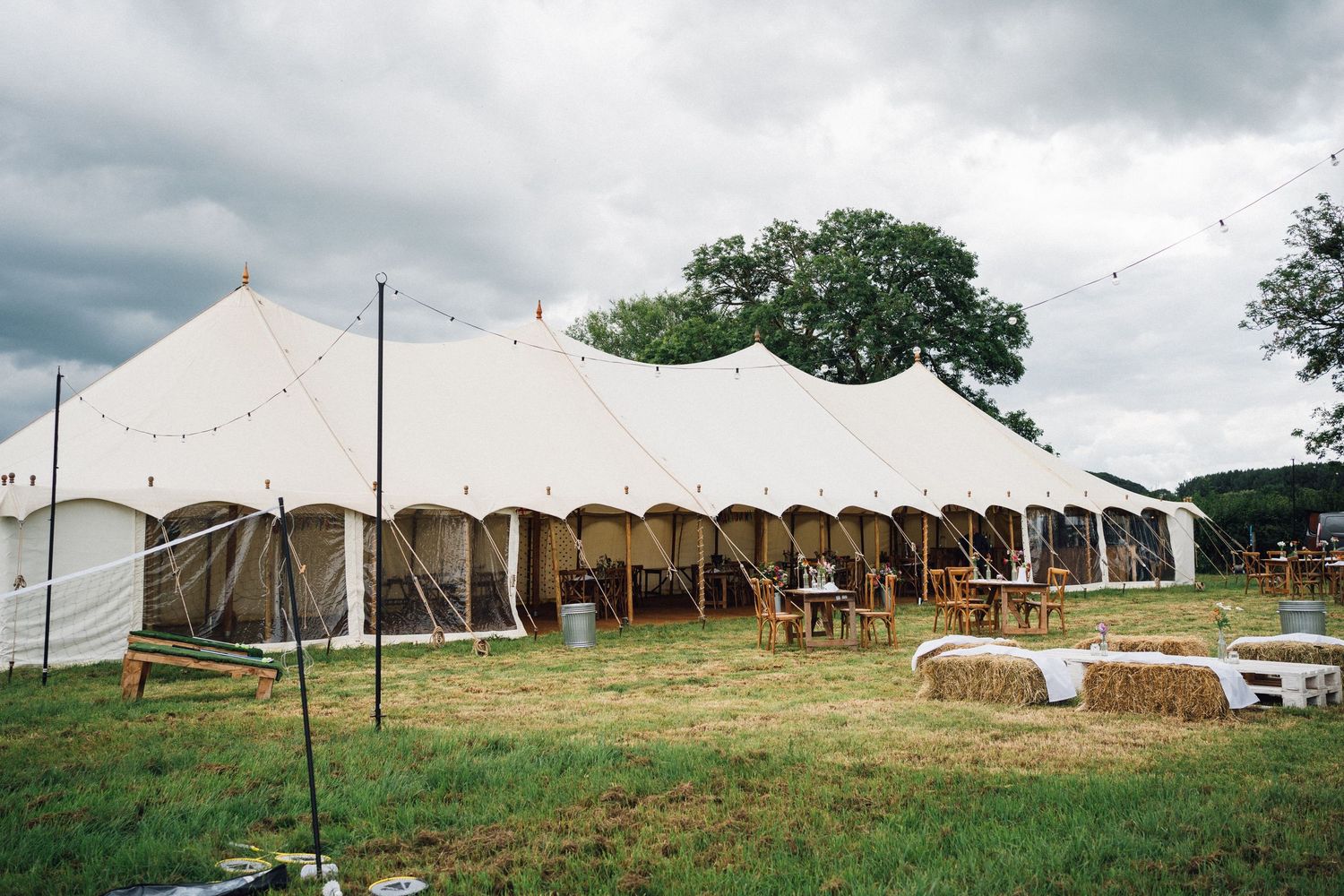 White event tents set up in a grassy field with hay bales and trees visible in the background.