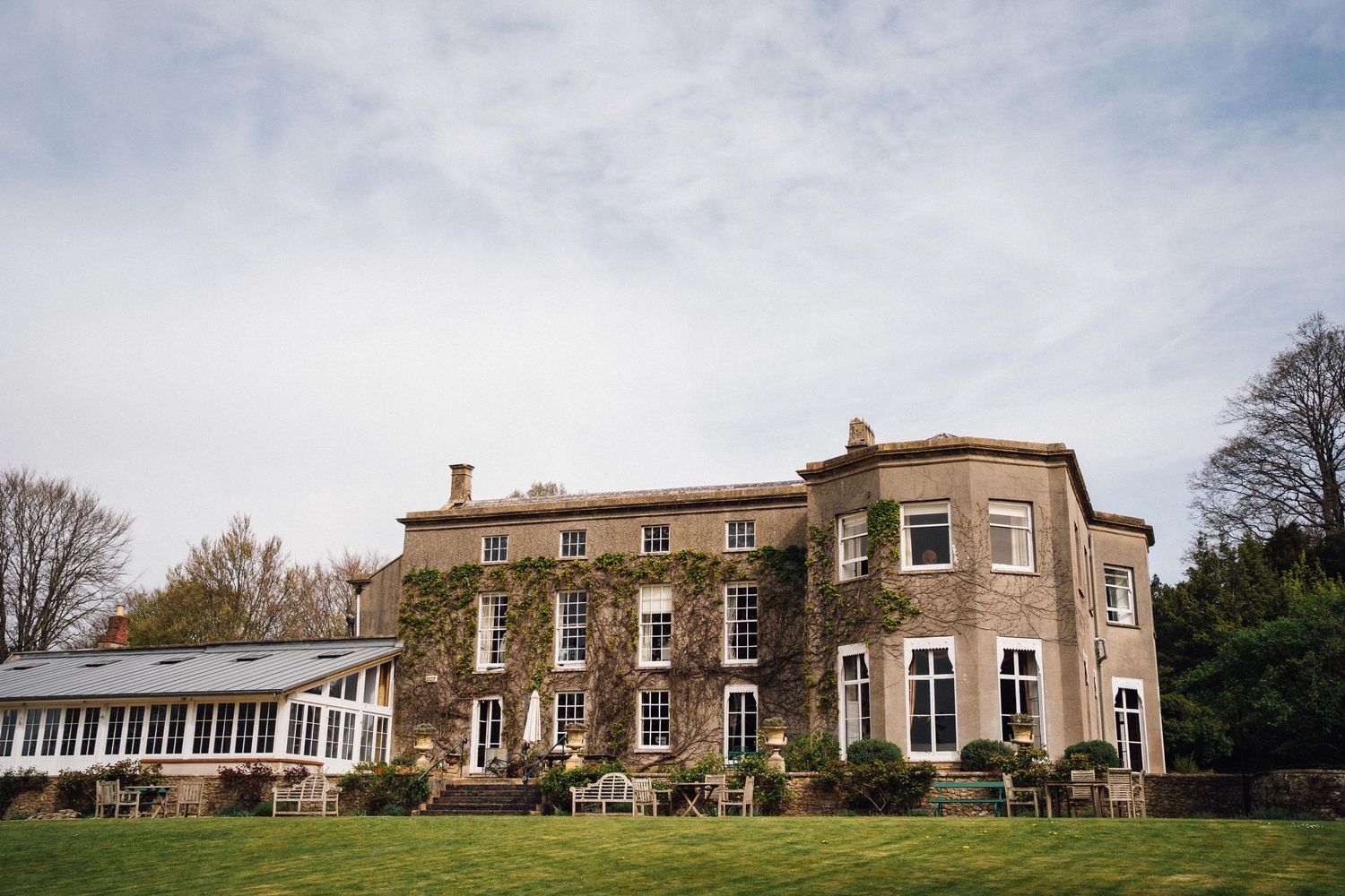 Panoramic view of a historic Georgian manor house with brick facade and surrounding gardens in the English countryside.