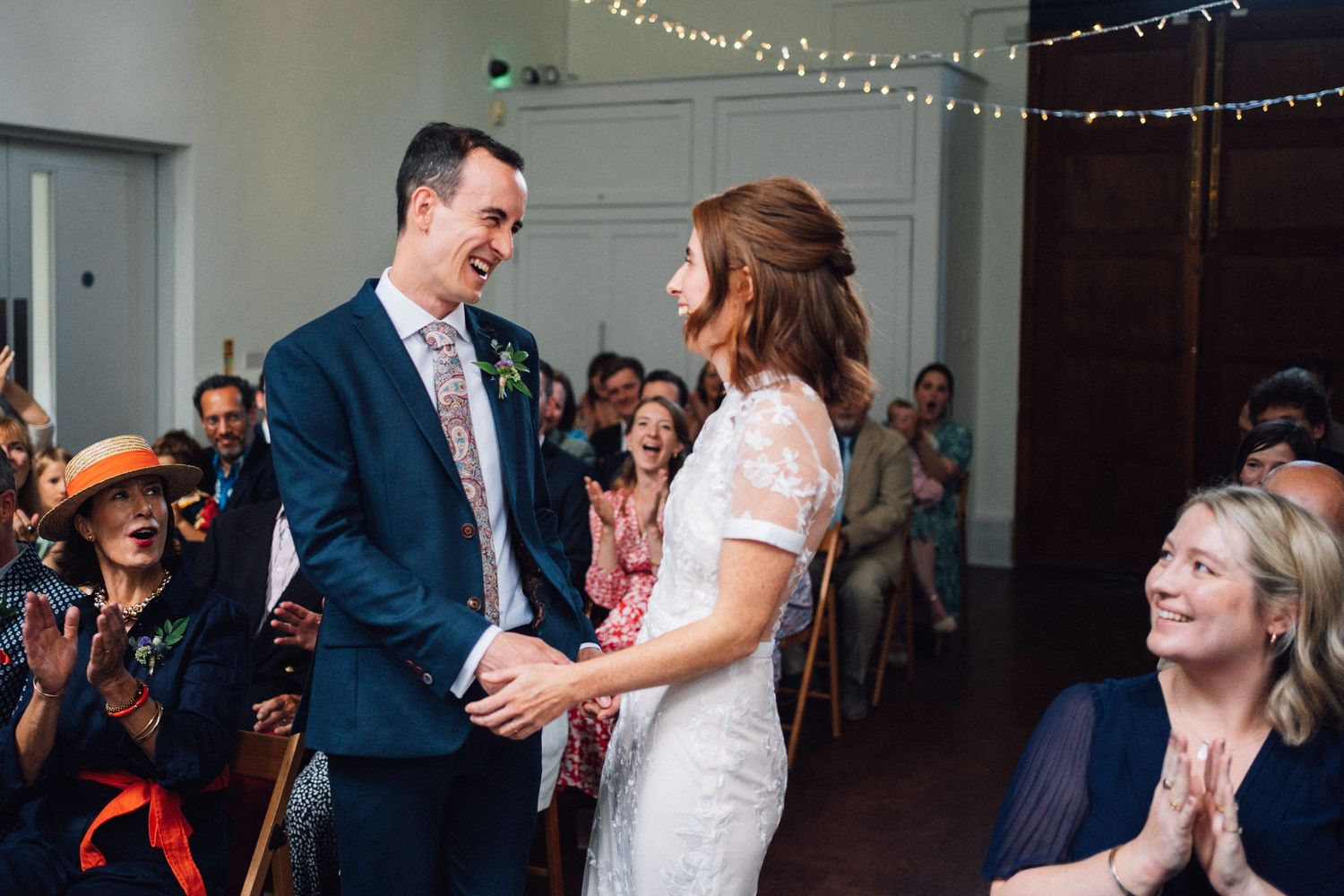 Wedding guests dance and celebrate during a joyful reception with twinkling lights in the background.