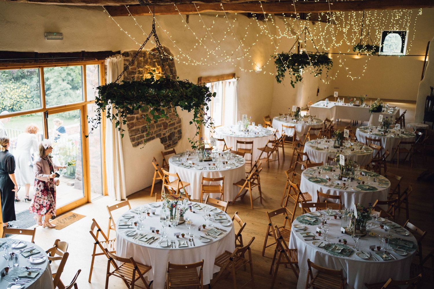 Wedding reception hall decorated with hanging greenery and round tables with white linens.
