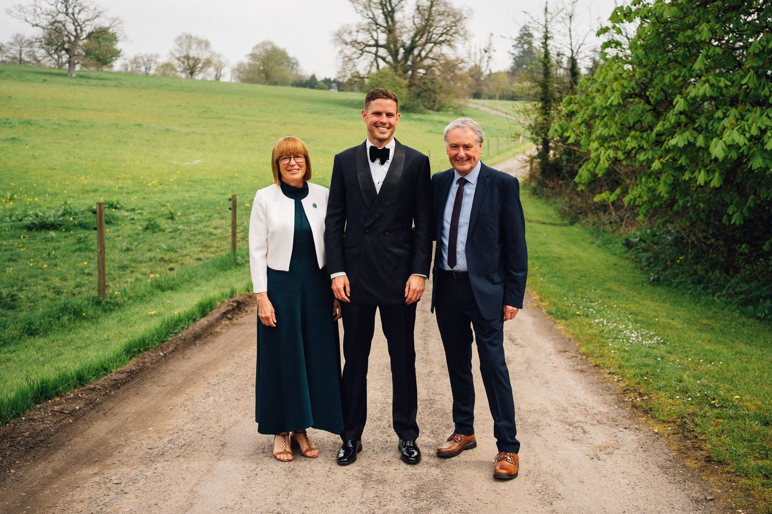 Groomsmen walking and posing together on a countryside path surrounded by green fields.