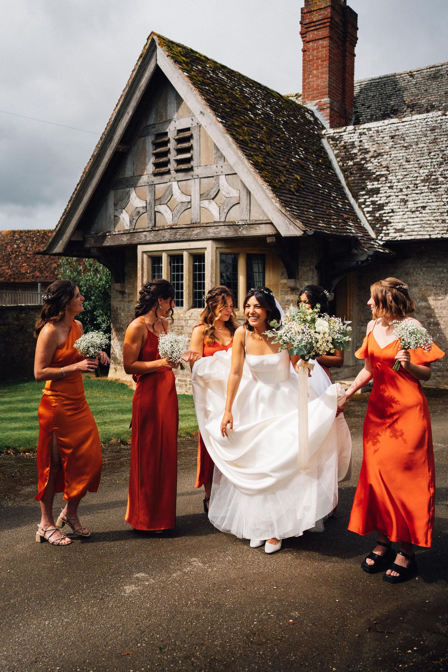 Wedding party with orange bridesmaid dresses posing outside a Tudor-style building.
