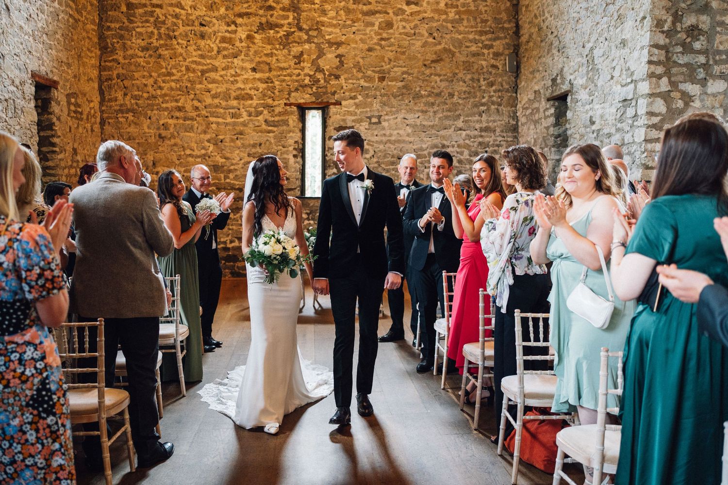 Wedding ceremony in rustic stone barn with rows of white chairs and natural lighting.