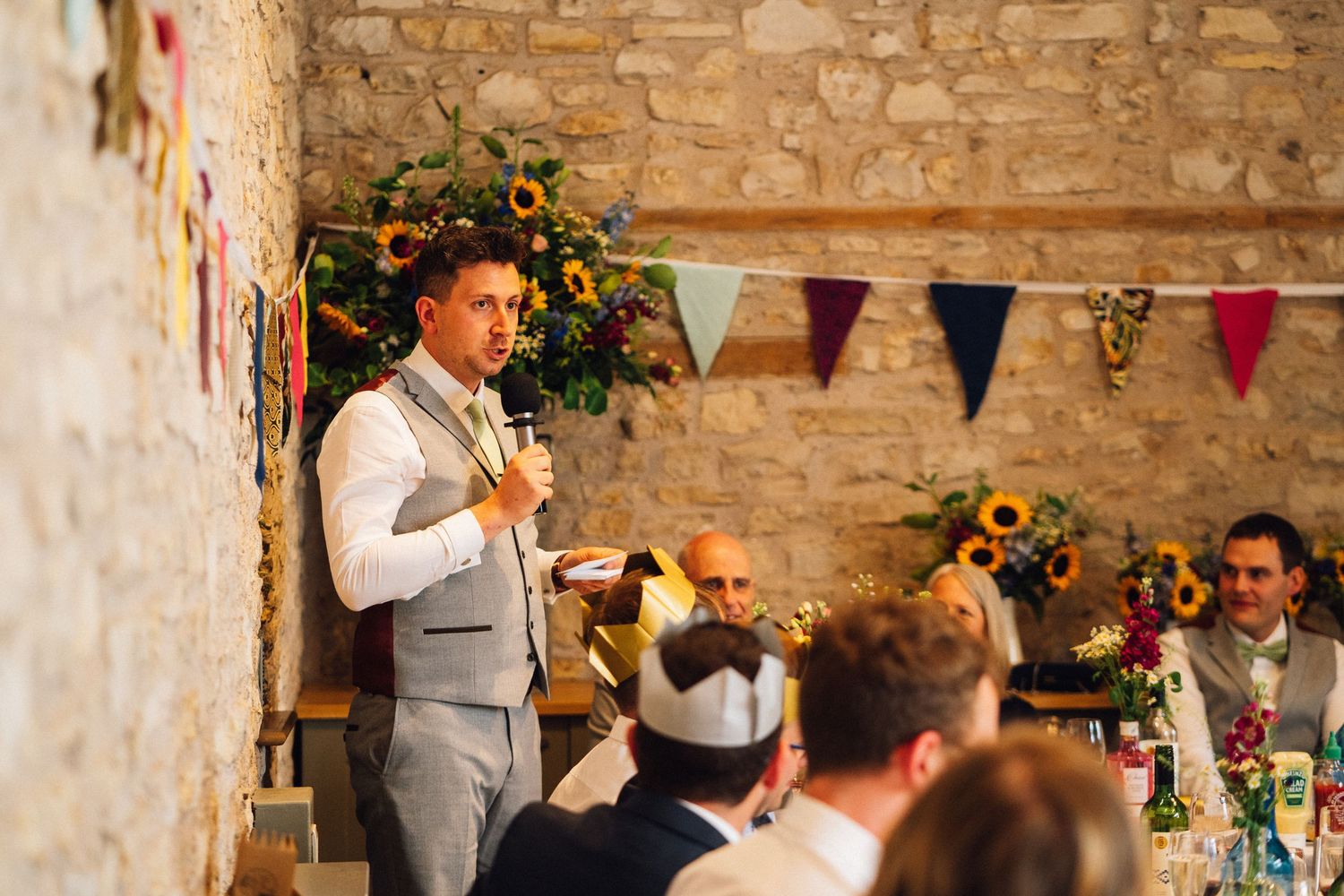 Wedding reception scene with decorative bunting and sunflowers against rustic stone walls.