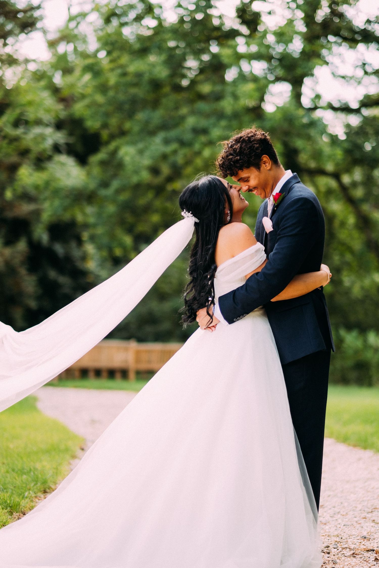 Wedding couple dancing on garden path with flowing white veil.