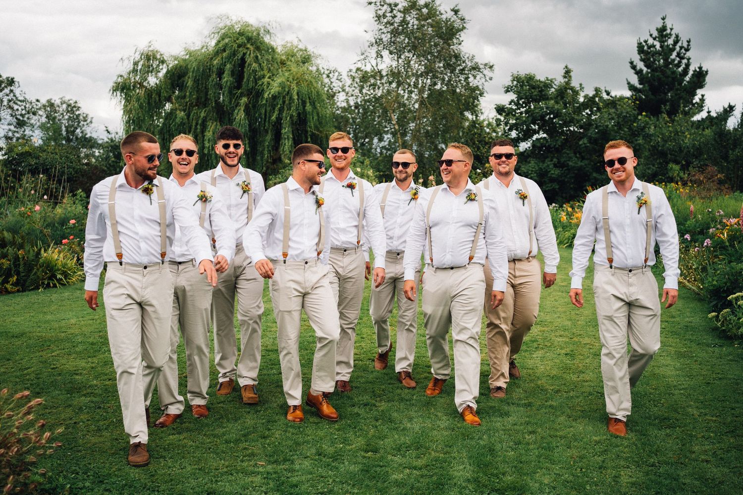 A wedding party in white attire poses together on a lush green lawn during an outdoor celebration.