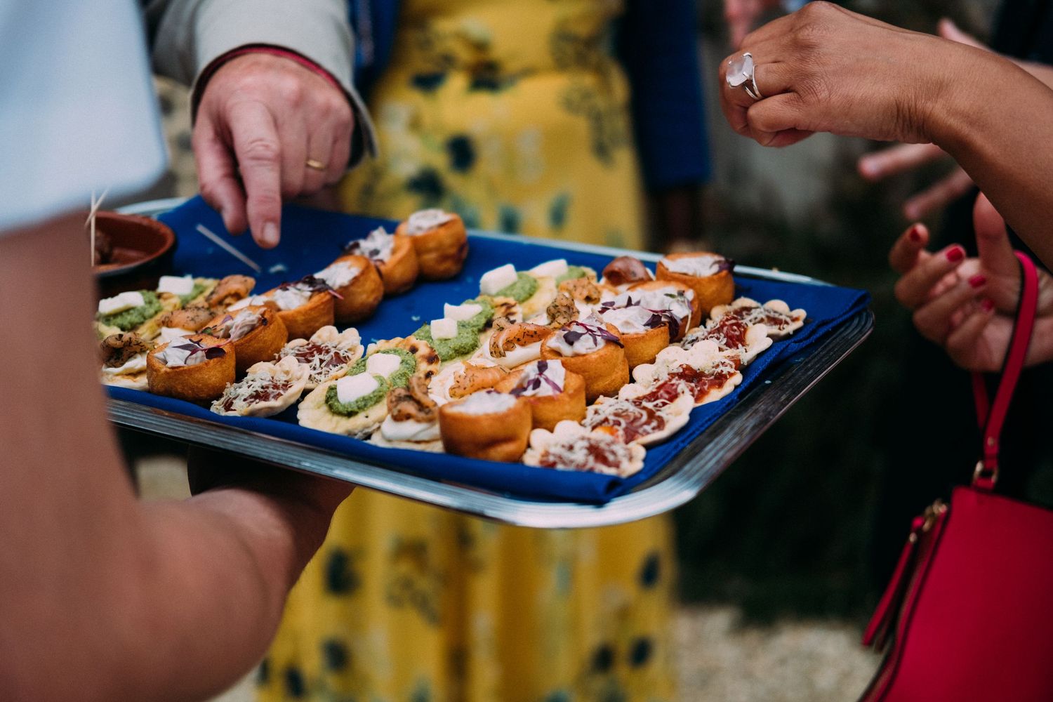 Catering staff serve appetizers on blue plates during an elegant outdoor event reception.