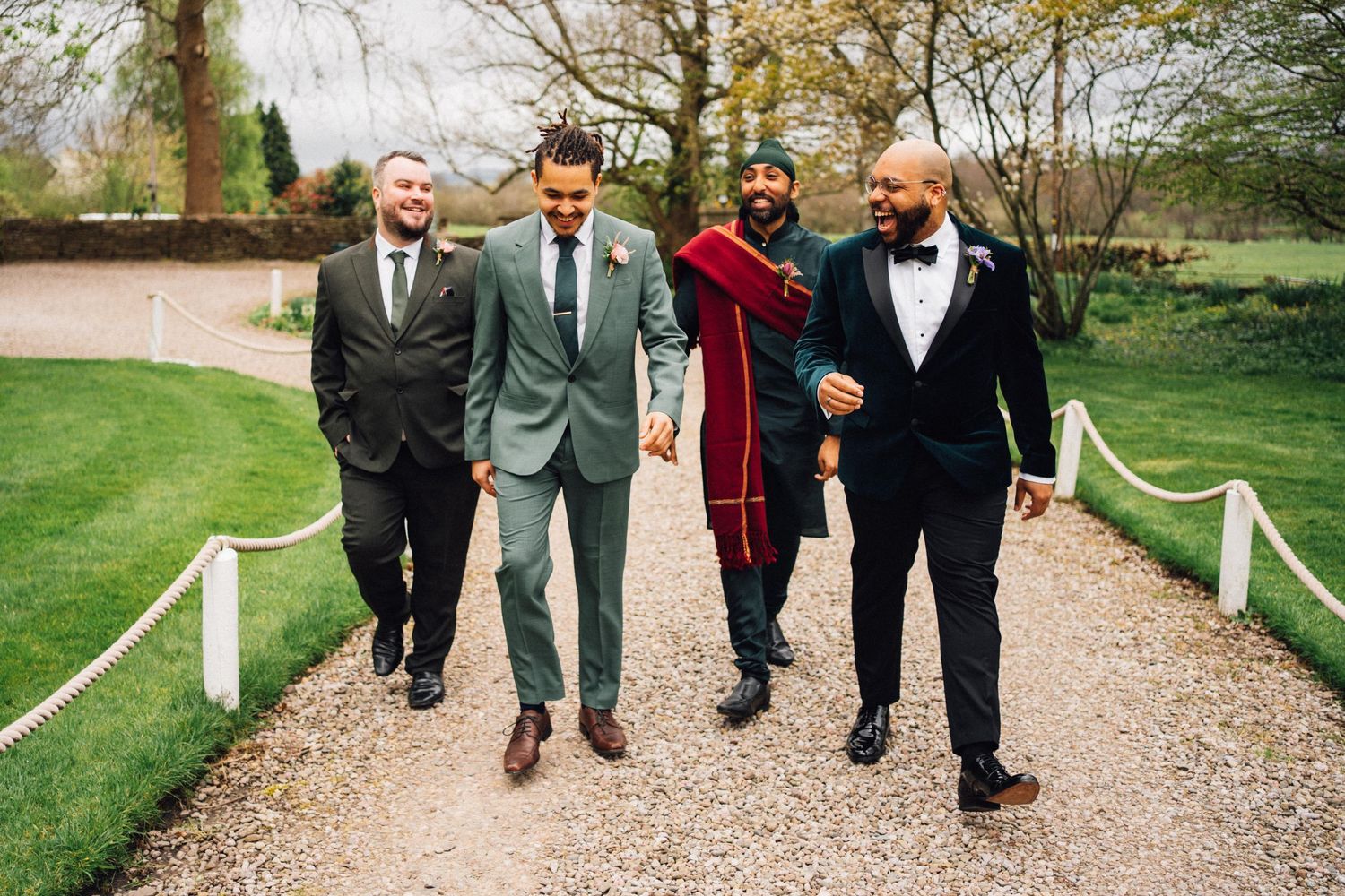 A group of well-dressed people walk together and laugh while strolling down a rope-lined garden path.