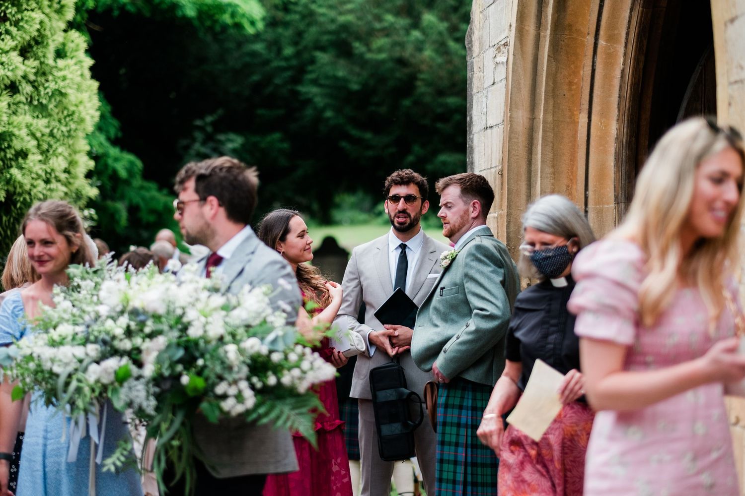 Wedding celebration outside historic church with stone archways and green foliage.