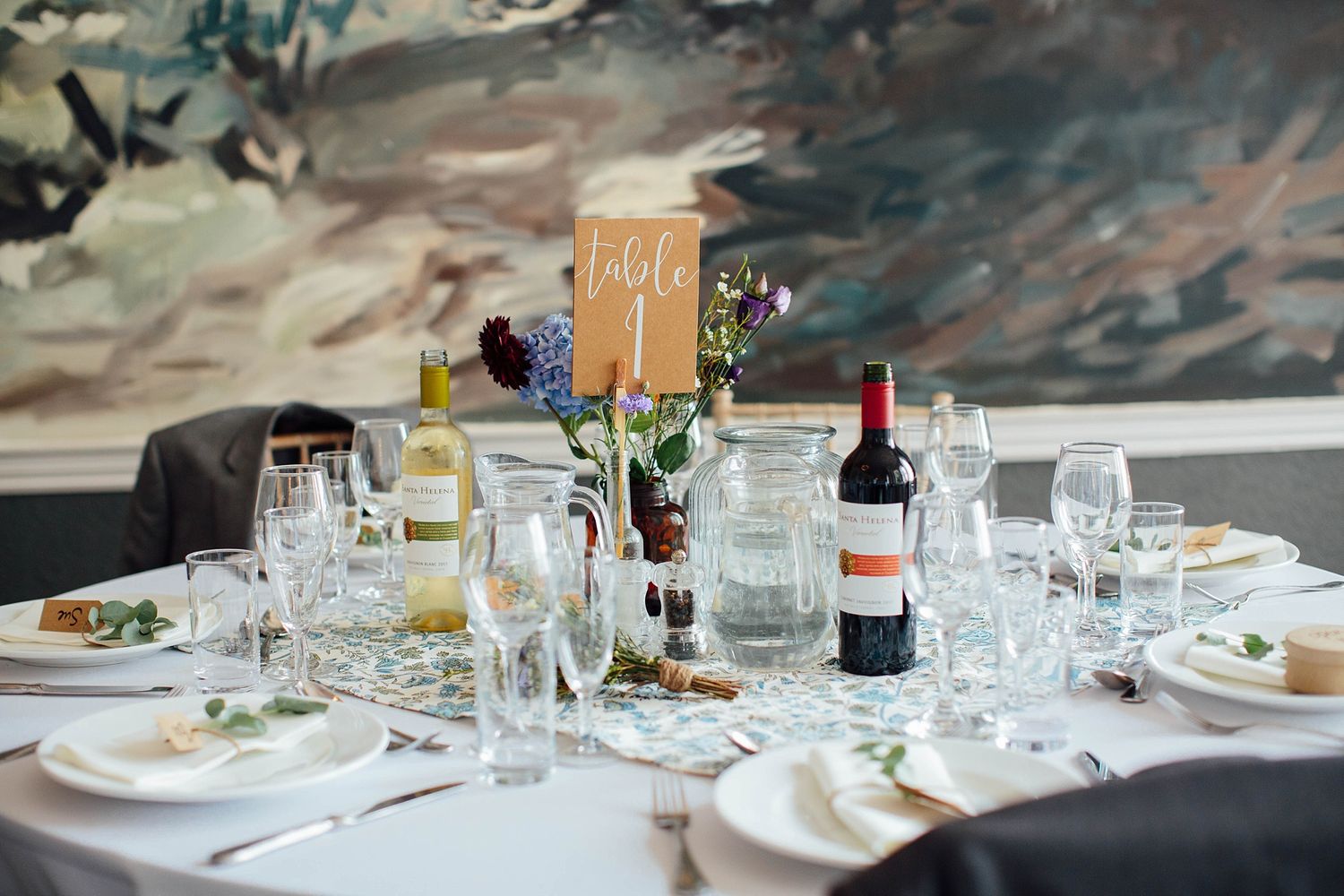 Wedding reception table setting with wine bottles, mason jars and place cards.