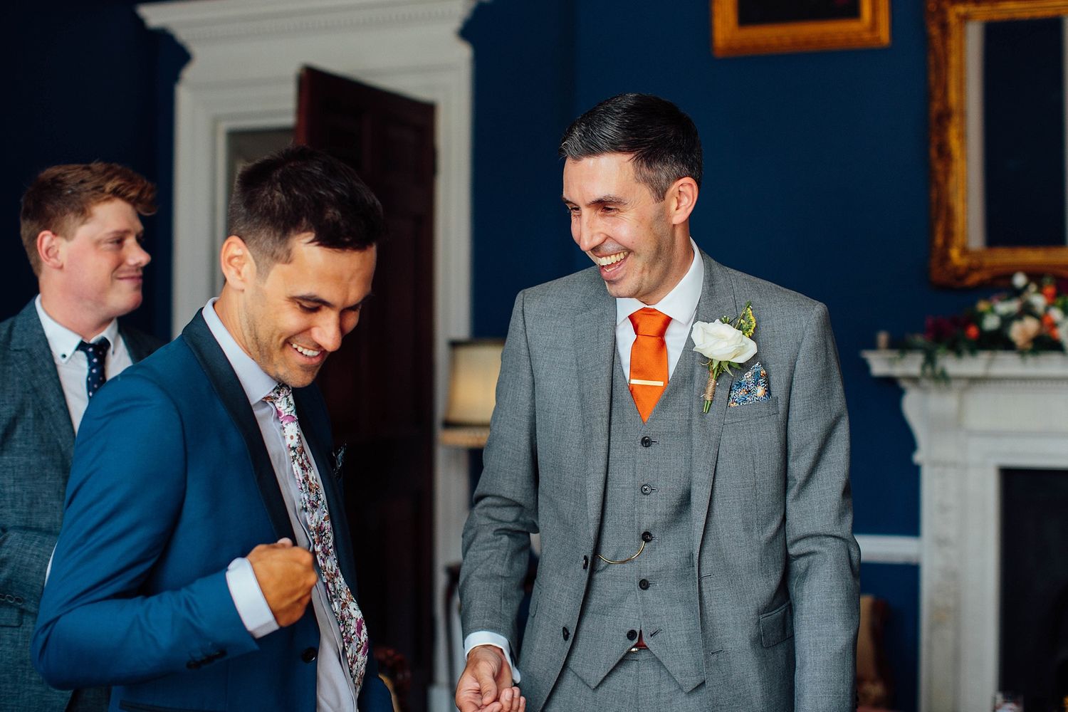 Groomsmen in navy and grey suits share laughs during wedding festivities.