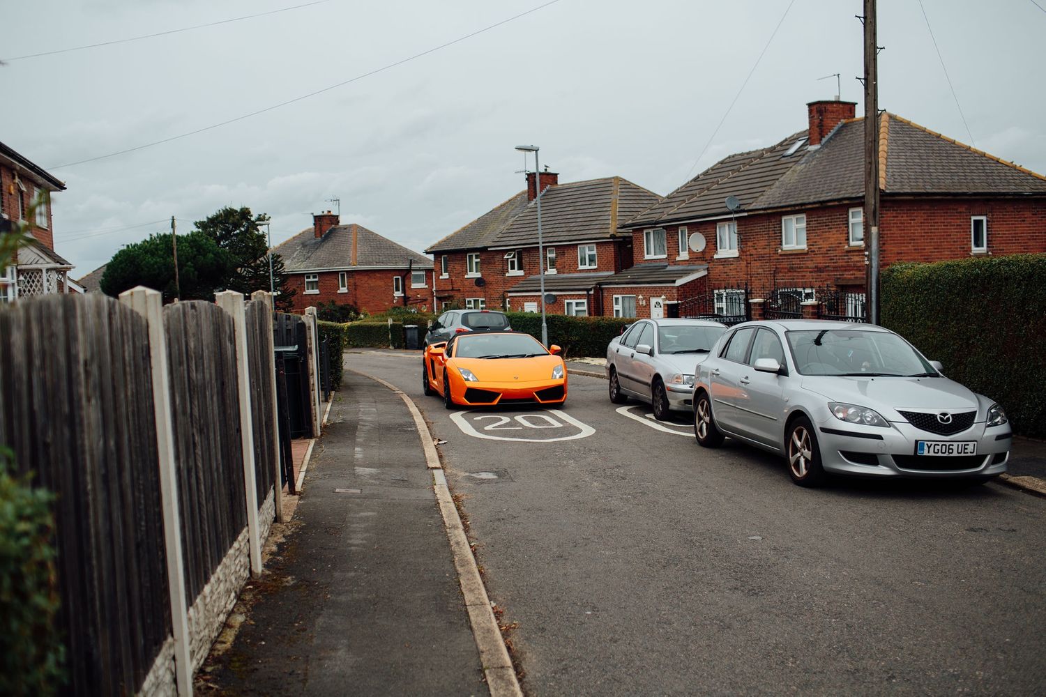 An orange sports car parked on a residential street among other vehicles.