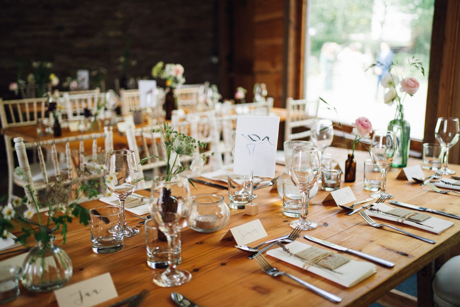 Elegant table settings at a wedding reception with glassware and greenery decorations.