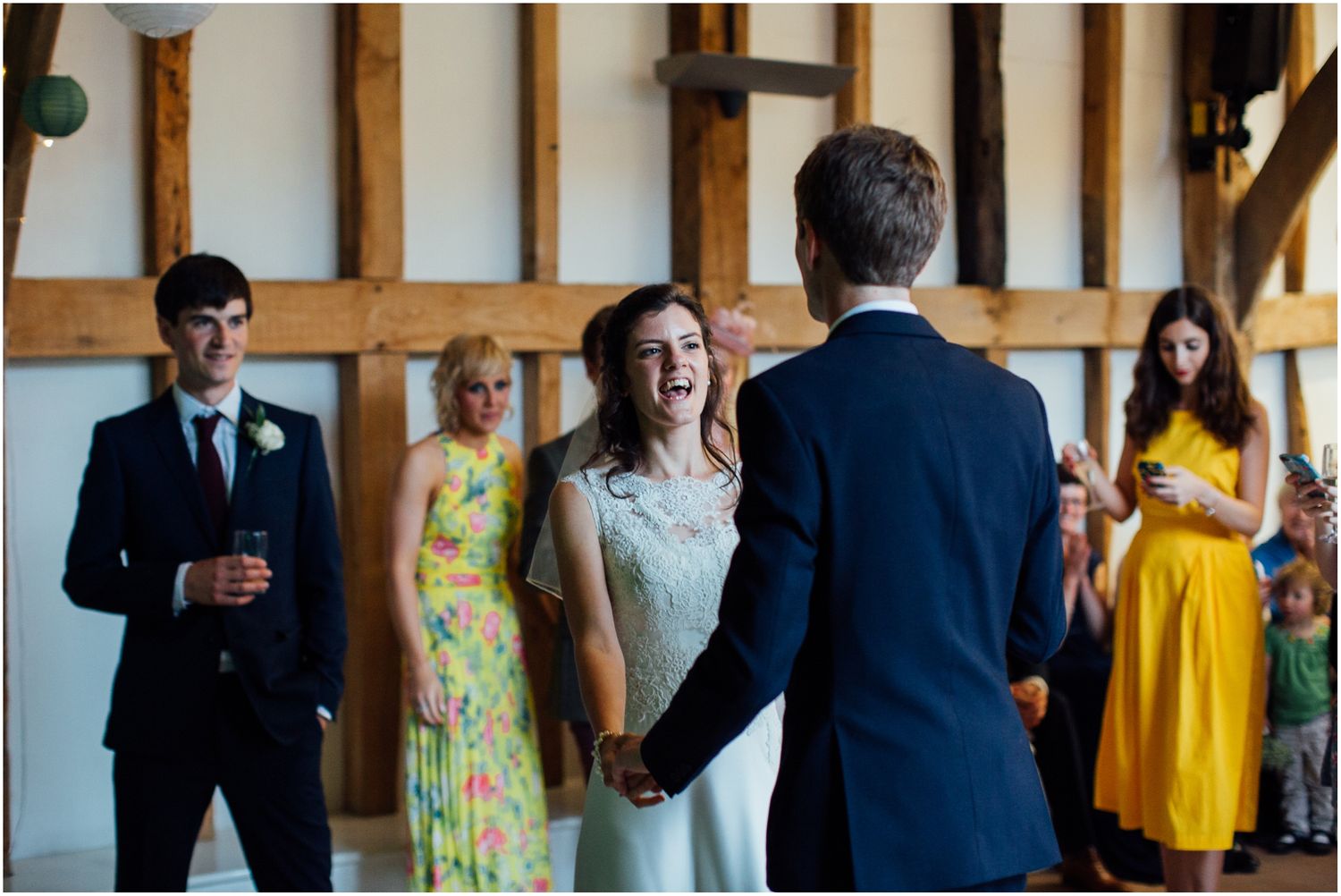 Wedding party members in formal attire gather during a celebration at a rustic venue with wooden beams.