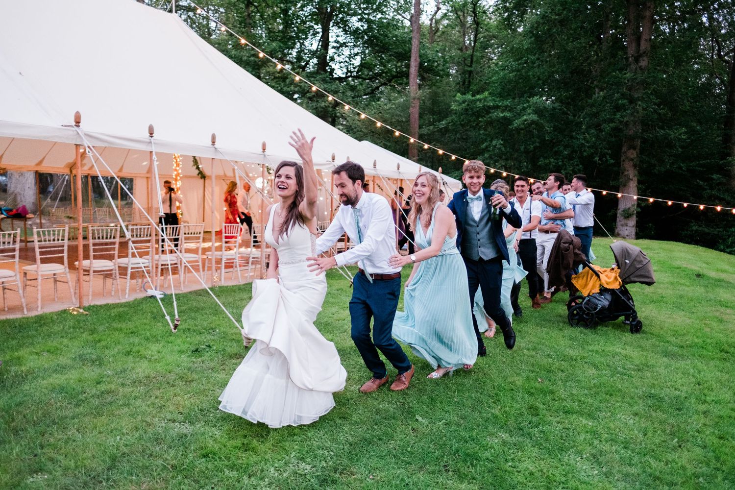Wedding guests play a fun game on the grass outside a white tent during an outdoor reception celebration.