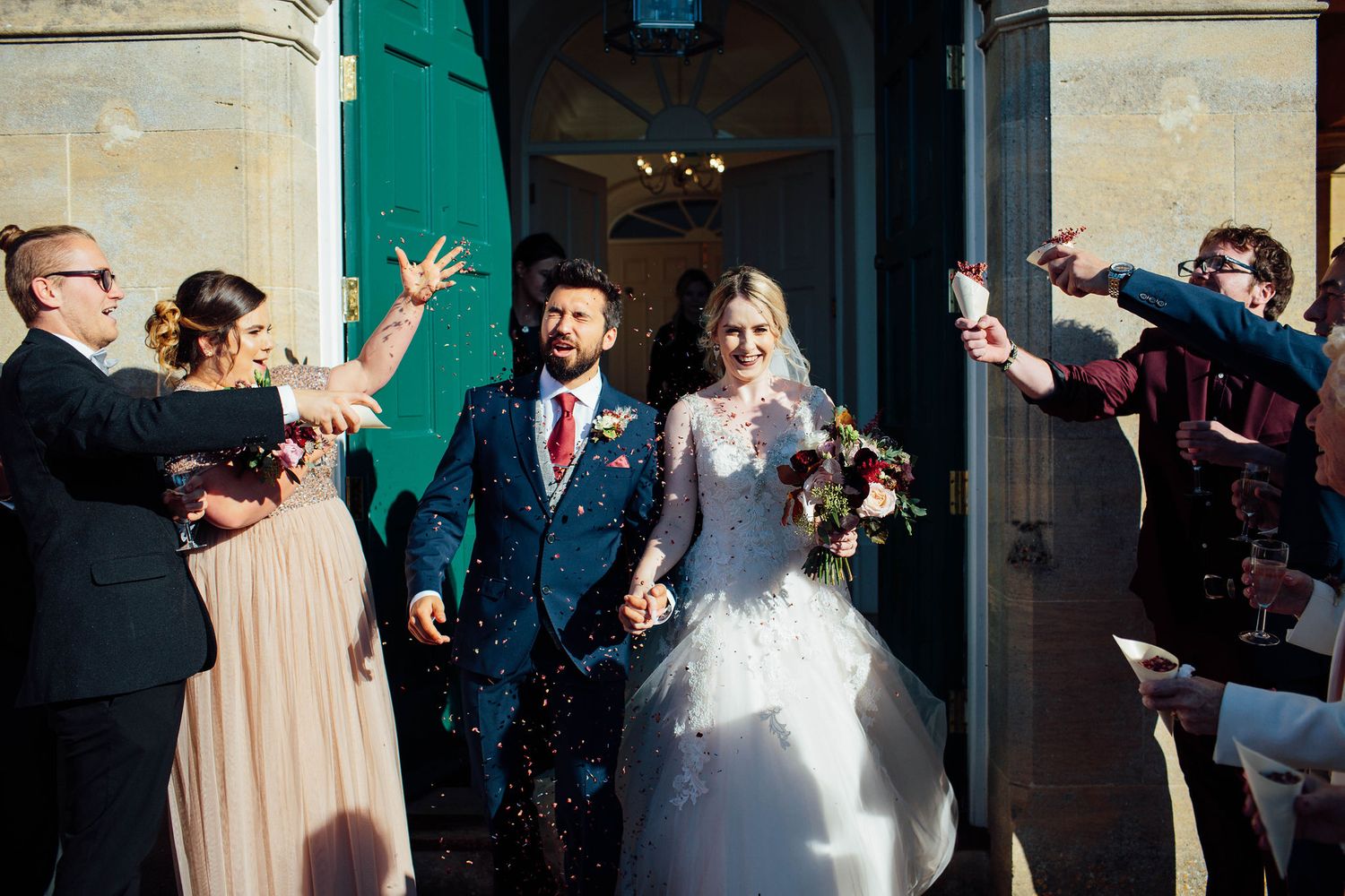 Wedding party and guests celebrate outside a historic building with teal shutters.