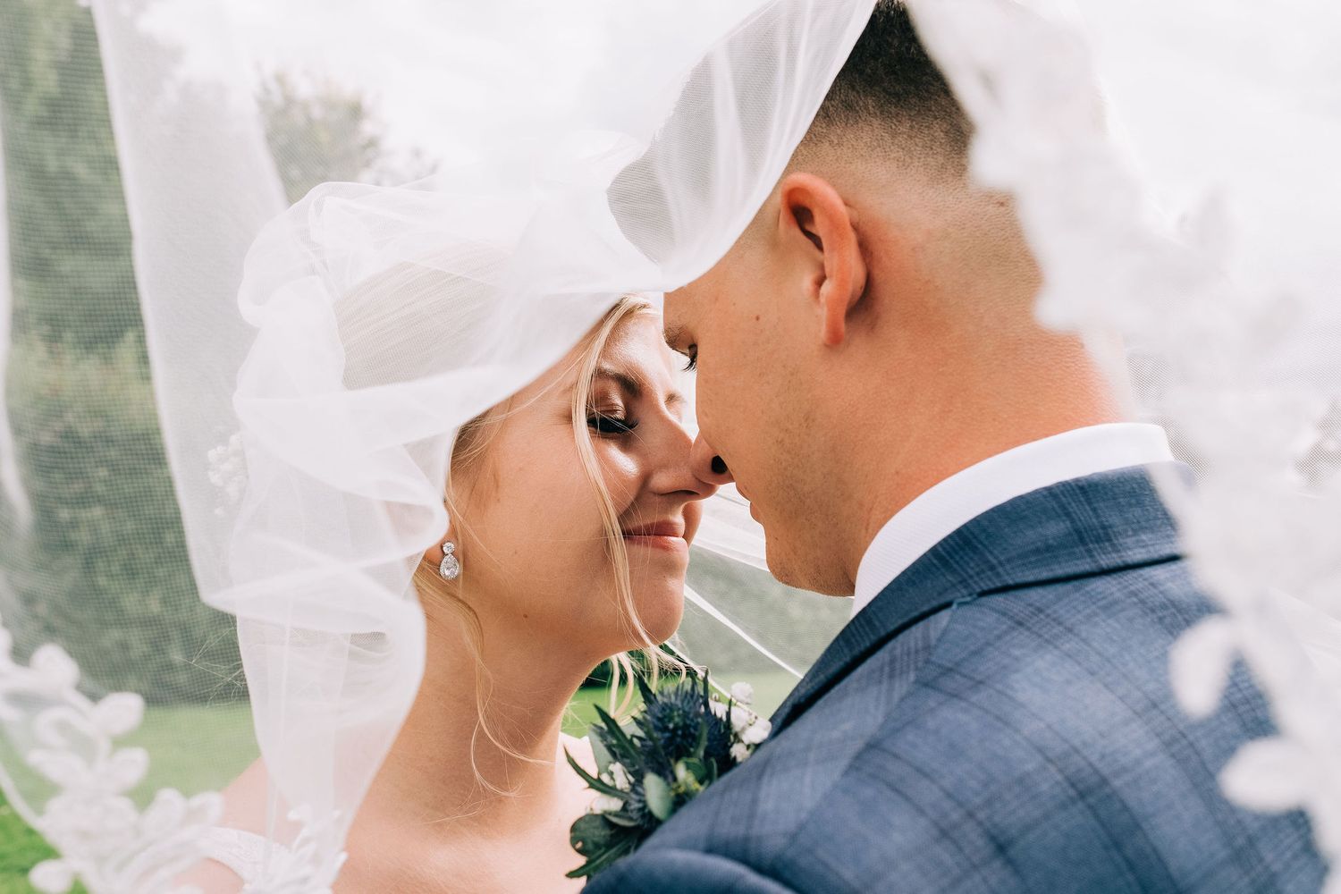 Close-up wedding moment with flowing veil against soft white background.