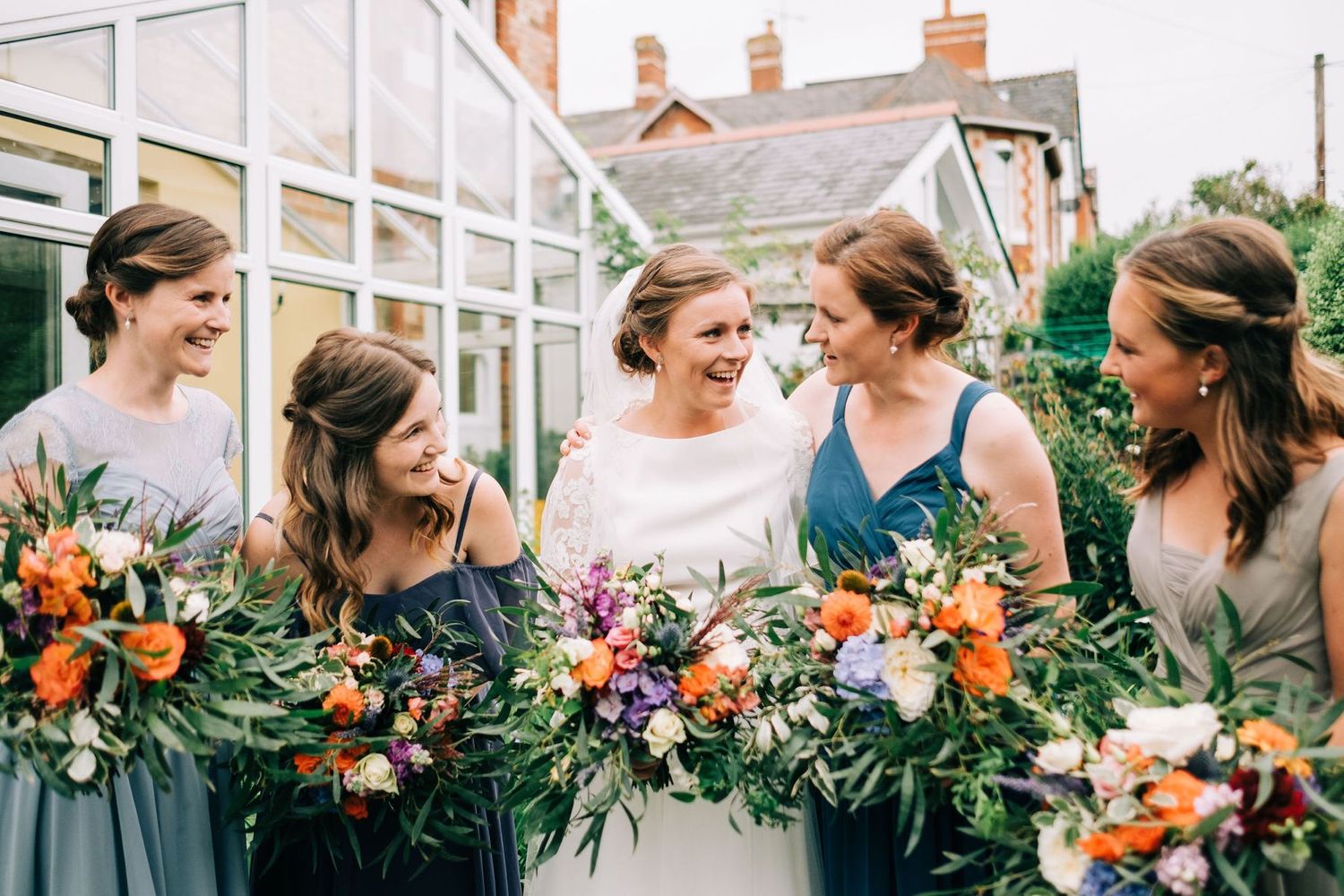 Wedding party holding vibrant orange and purple floral bouquets in an outdoor setting.