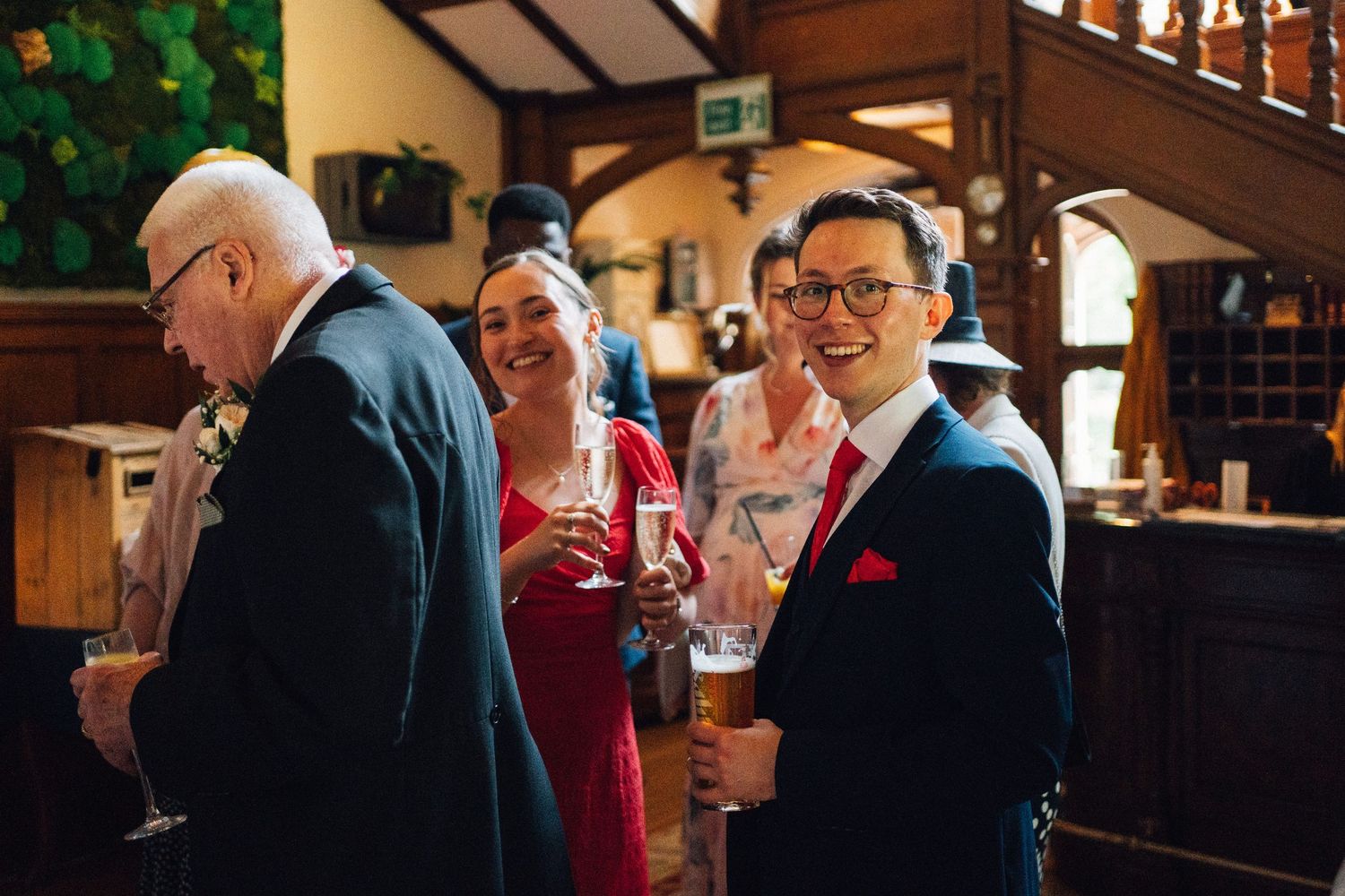 Guests socializing at a wedding reception bar, smiling and holding drinks in a warmly lit venue.