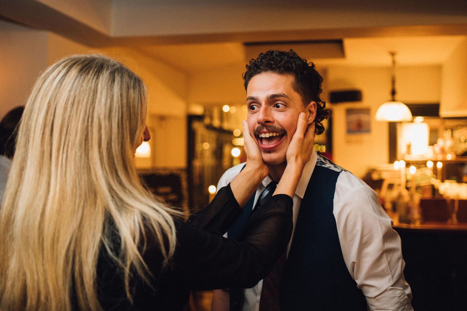 Two restaurant workers share an enthusiastic moment during their shift in a warmly lit dining establishment.