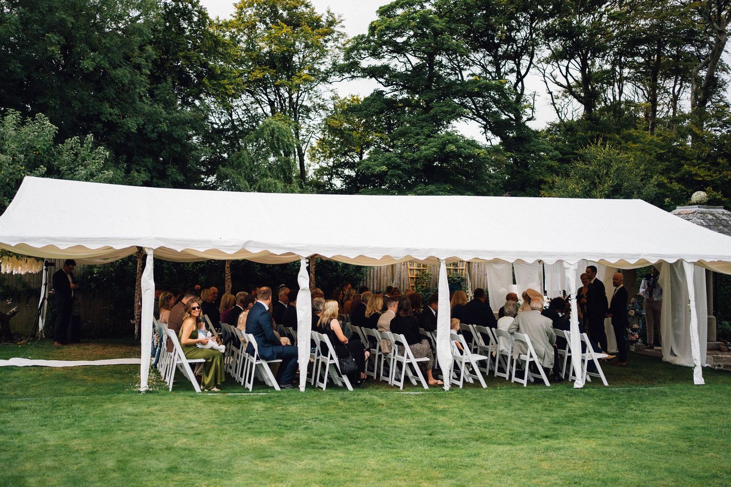 White wedding tent set up on expansive lawn with rows of chairs for outdoor ceremony.