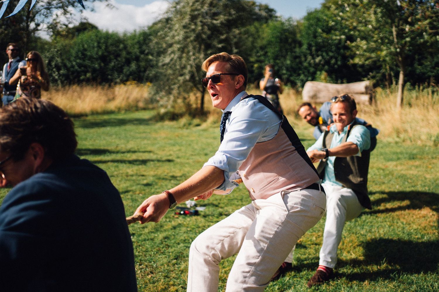 Group of people playing tug of war on a sunny grassy field during an outdoor event.