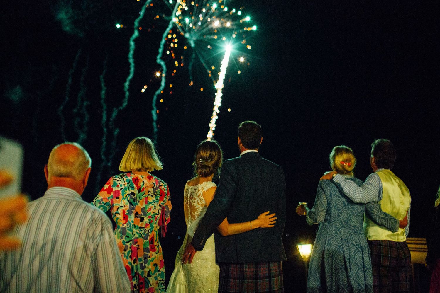 Silhouettes of wedding guests watching fireworks display against a night sky.