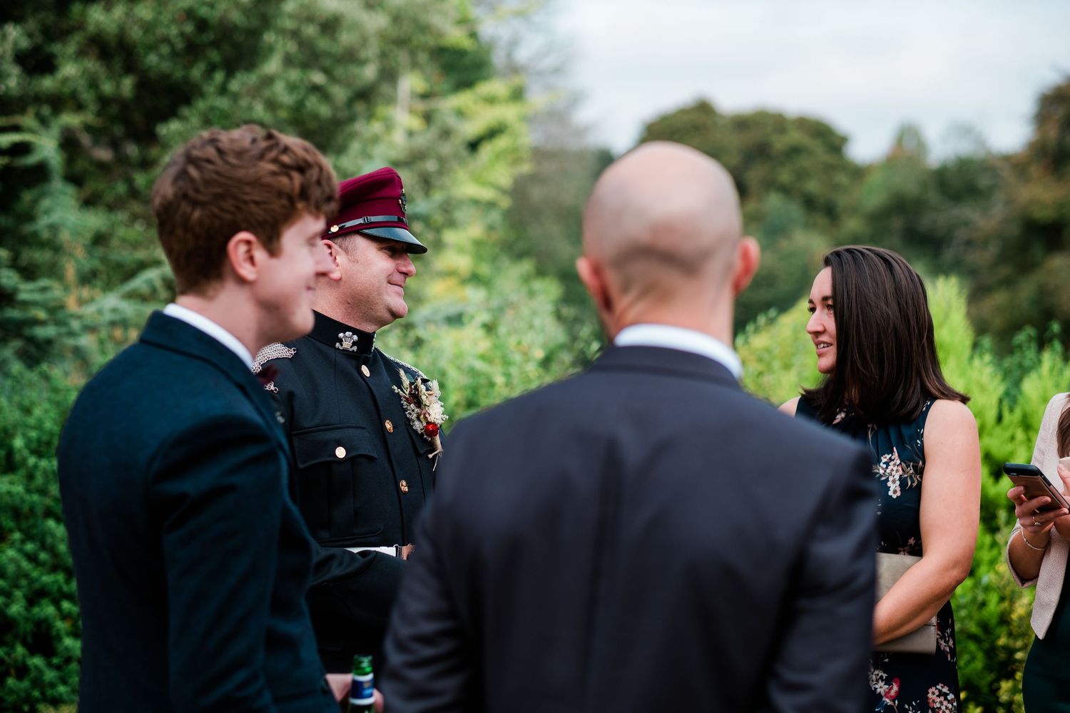 Wedding guests gather outdoors in formal attire among beautiful garden landscaping.