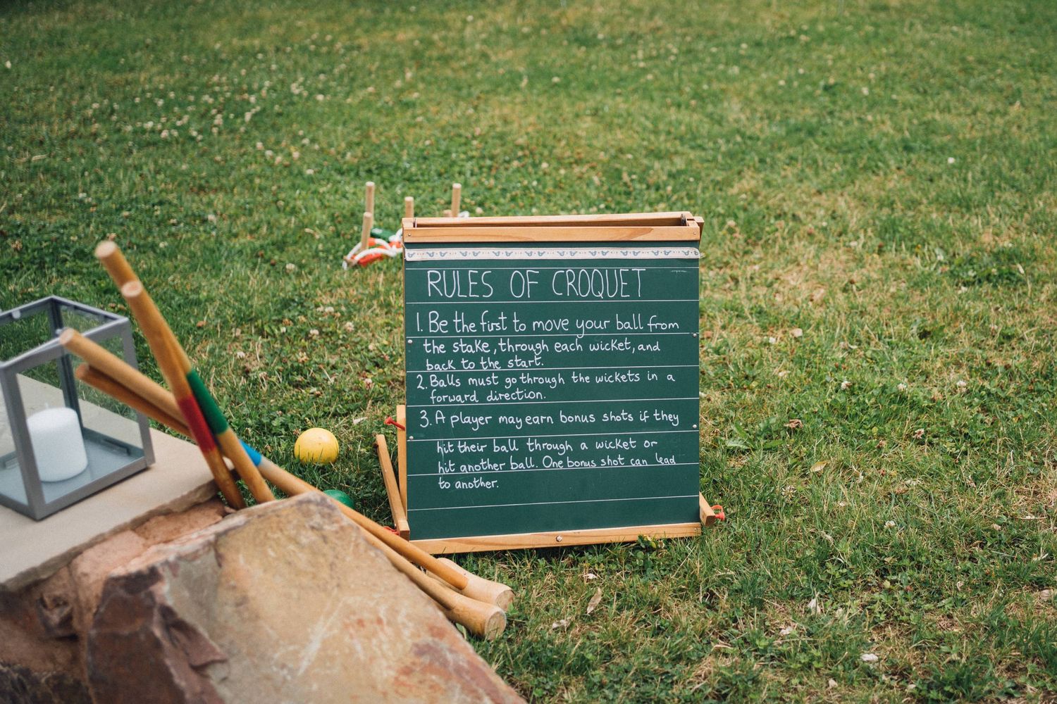 A chalkboard with wedding rules displayed on grass with decorative elements.